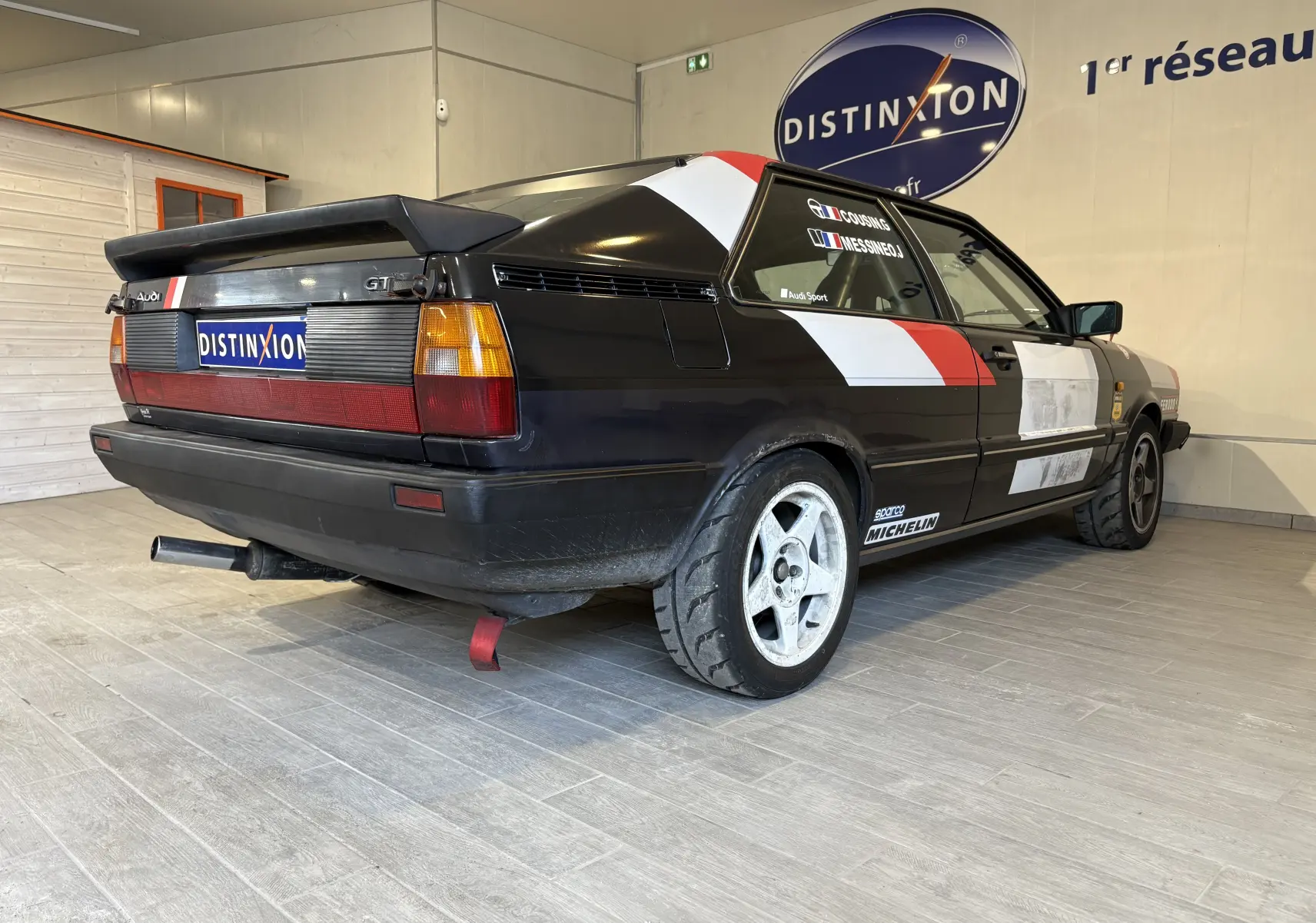 Vue intérieure côté conducteur de l'Audi Coupé GT noir de 1983, avec sièges baquets, harnais rouge et volant course.