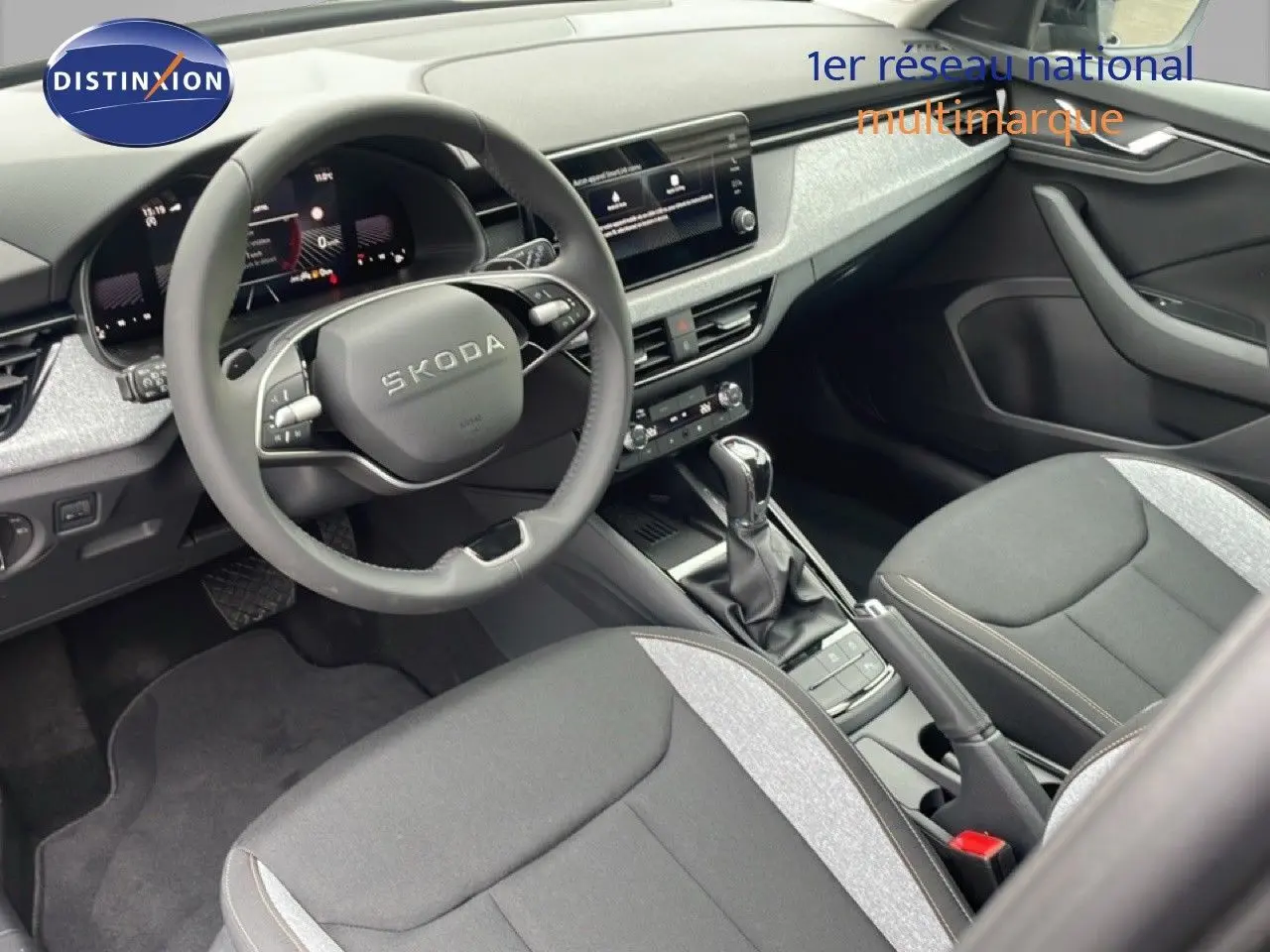 Intérieur avant du Skoda Kamiq 2025, vue côté conducteur, tableau de bord moderne et sièges tissu noir et gris.