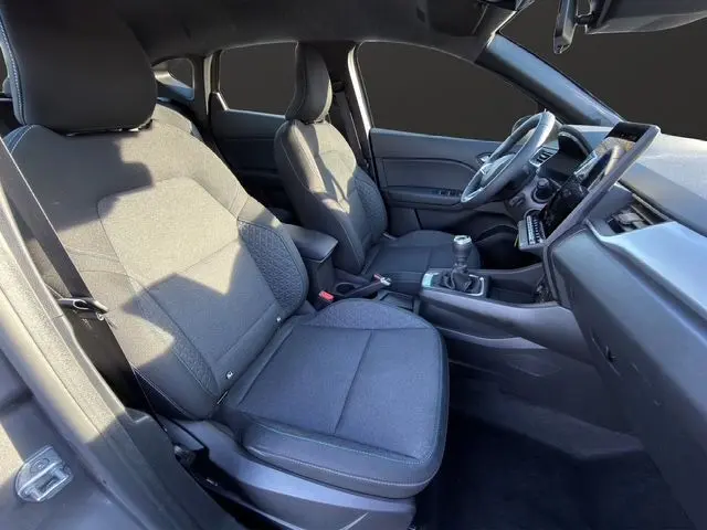 Intérieur avant du Renault Captur 2024, sièges tissu gris, volant tissu et boîte manuelle visible côté droit.