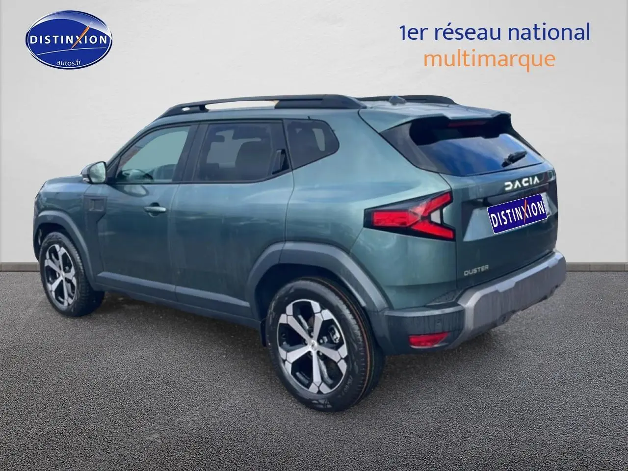 Vue 3/4 arrière droite du Dacia Duster 2026 vert cèdre avec barres de toit et jantes alu distinctives.