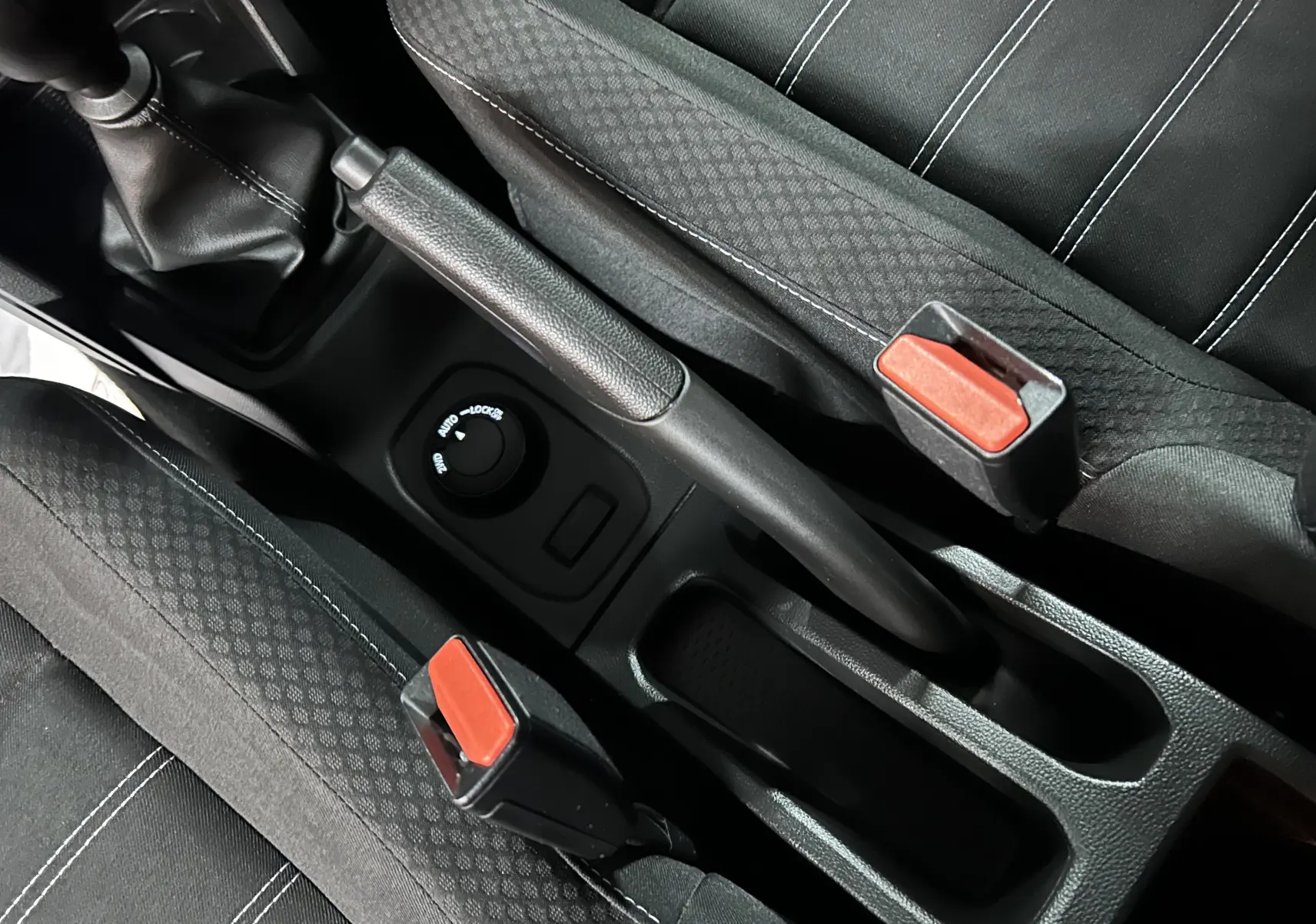 Vue rapprochée de la console centrale du Dacia Duster 2025, montrant frein à main, bouton 4x4 et ceintures noires.