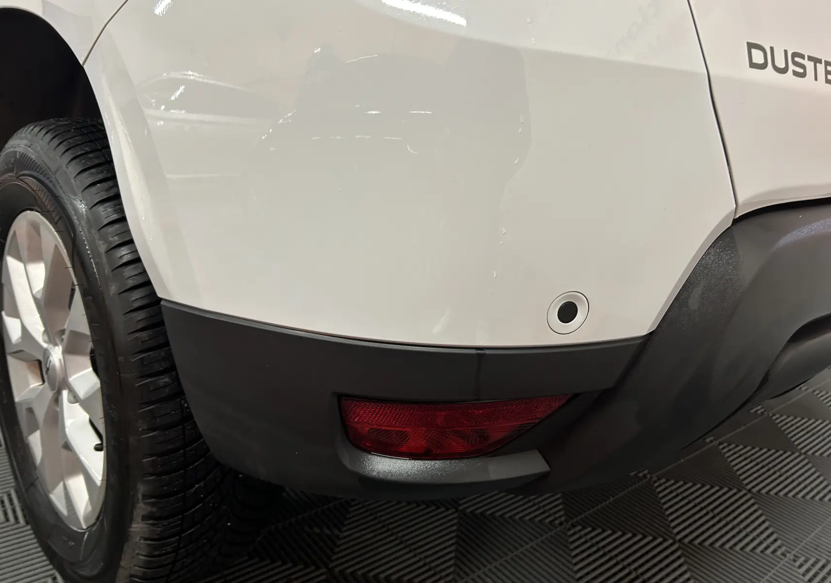 Gros plan sur l'arrière droit blanc du Dacia Duster 2025, avec feu rouge et capteur de stationnement visible.