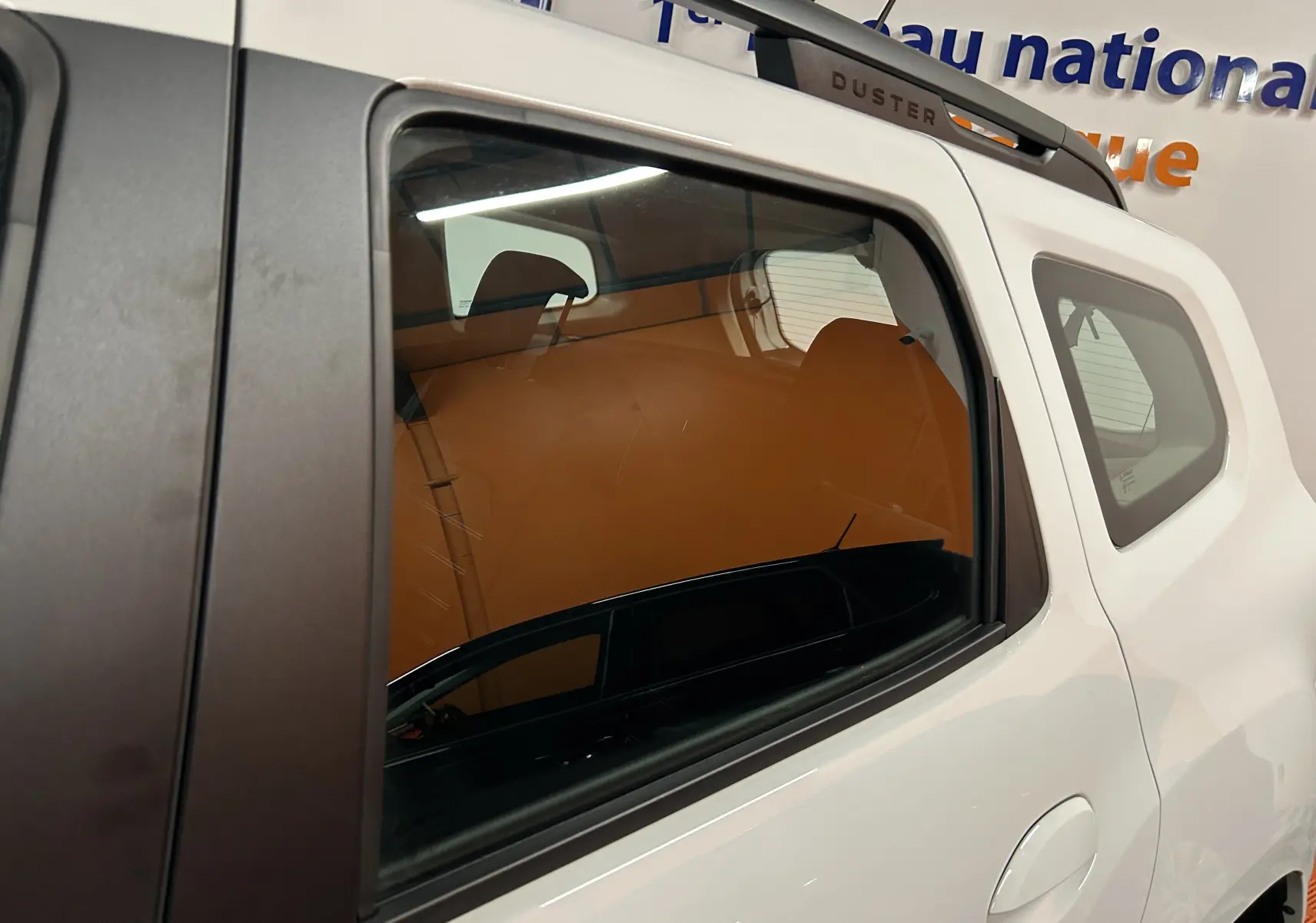 Vue latérale droite sur la partie arrière d'un Dacia Duster blanc 2025 avec toit noir et barres de toit Duster visibles.