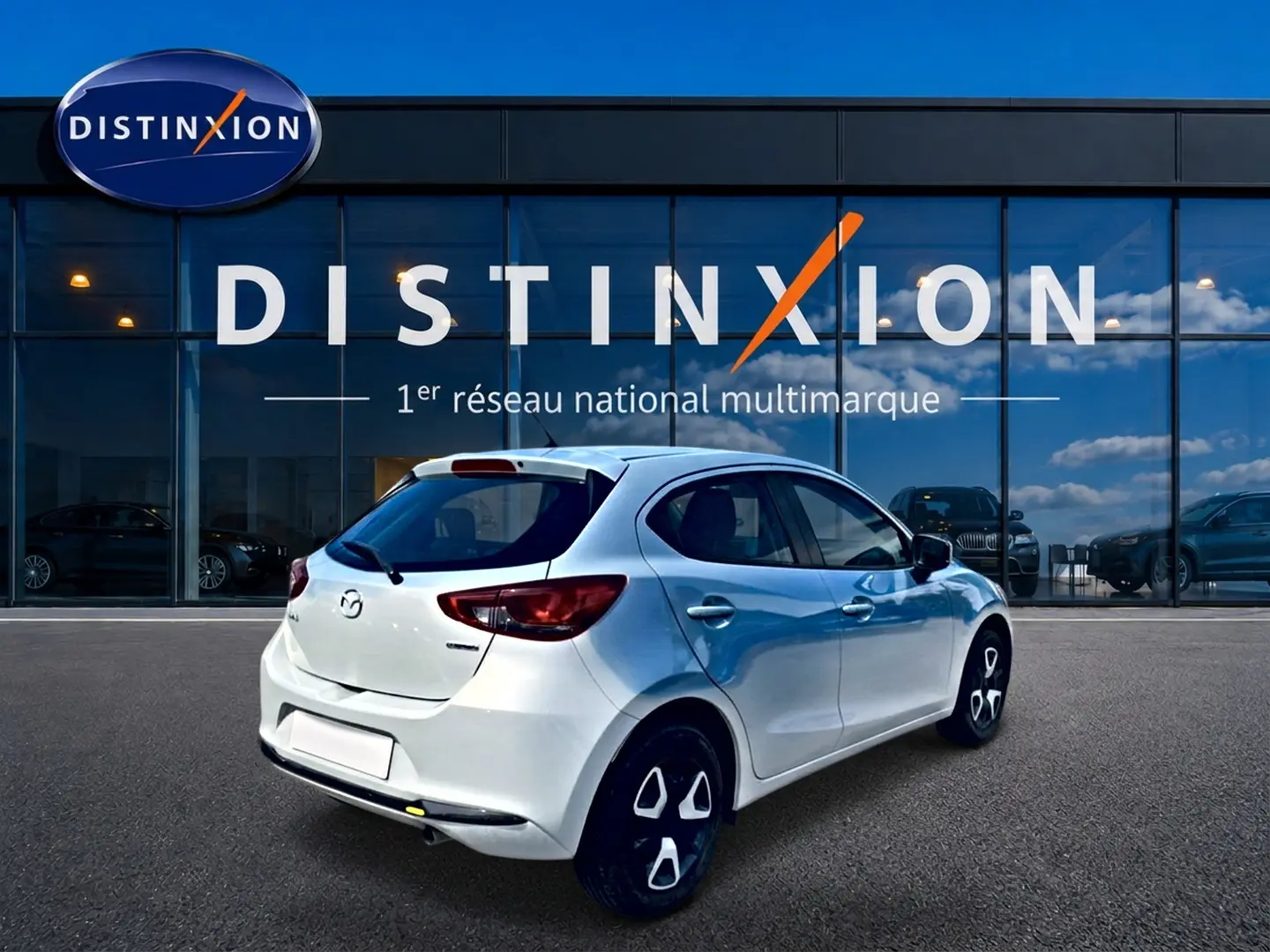 Vue 3/4 arrière droite d'une Mazda2 blanche 2024 stationnée devant une vitrine Distinxion.