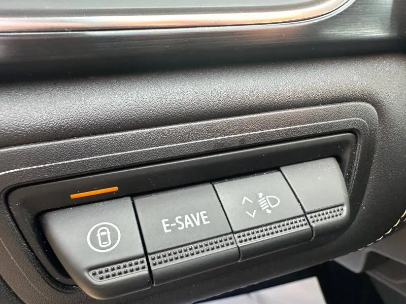 Gros plan sur les boutons de commande noirs du tableau de bord du Renault Symbioz rouge, avec fonction E-SAVE et réglage des phares.