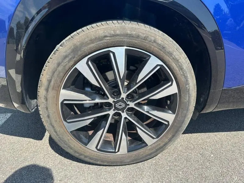 Gros plan sur la roue avant droite du Renault Austral bleu Iron avec jante alu noire et argentée.