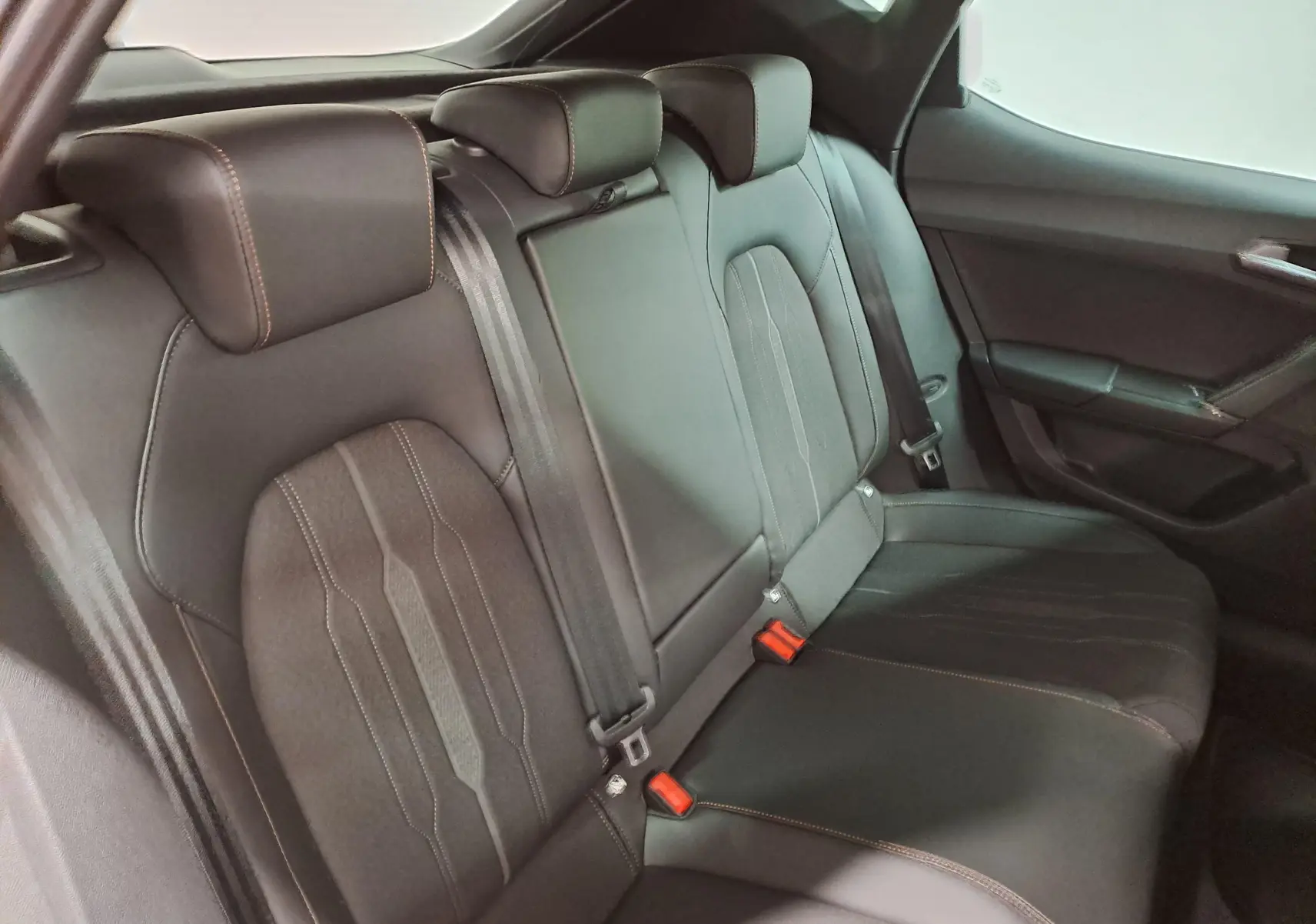 Vue intérieure du siège arrière droit de la CUPRA Leon 2023 en cuir noir avec surpiqûres orange et ceintures de sécurité.