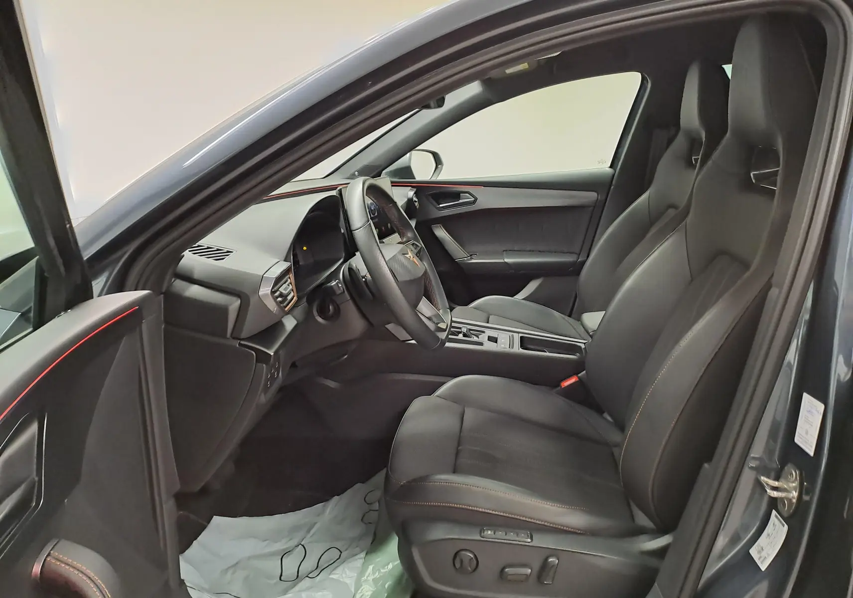 Vue intérieure côté conducteur de la CUPRA Leon 2023 avec sièges sport noirs et surpiqûres orange, tableau de bord moderne.