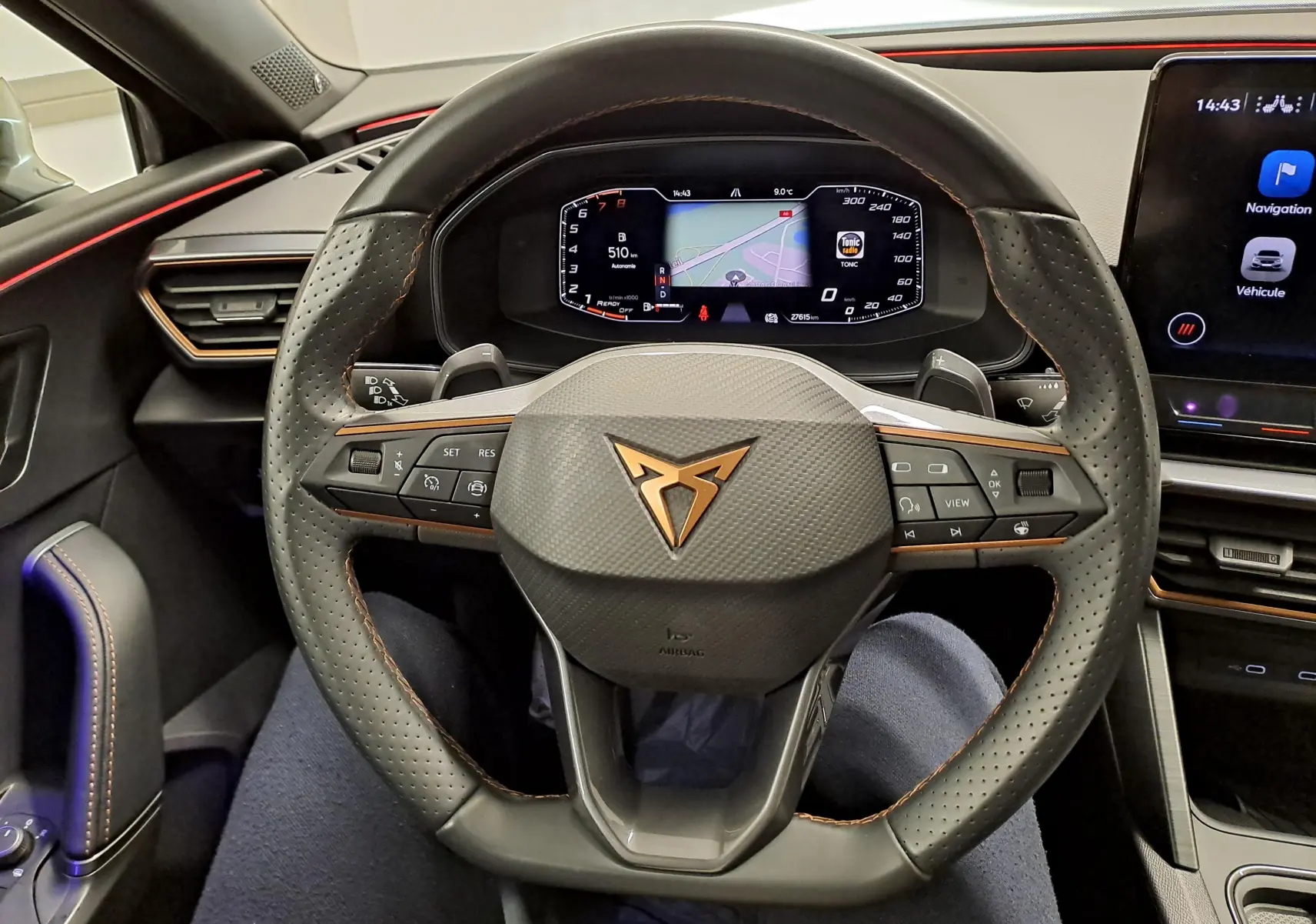 Vue intérieure centrée sur le volant perforé de la CUPRA Leon 1.5 TSI 150 DS7 V avec logo cuivré et tableau de bord numérique.