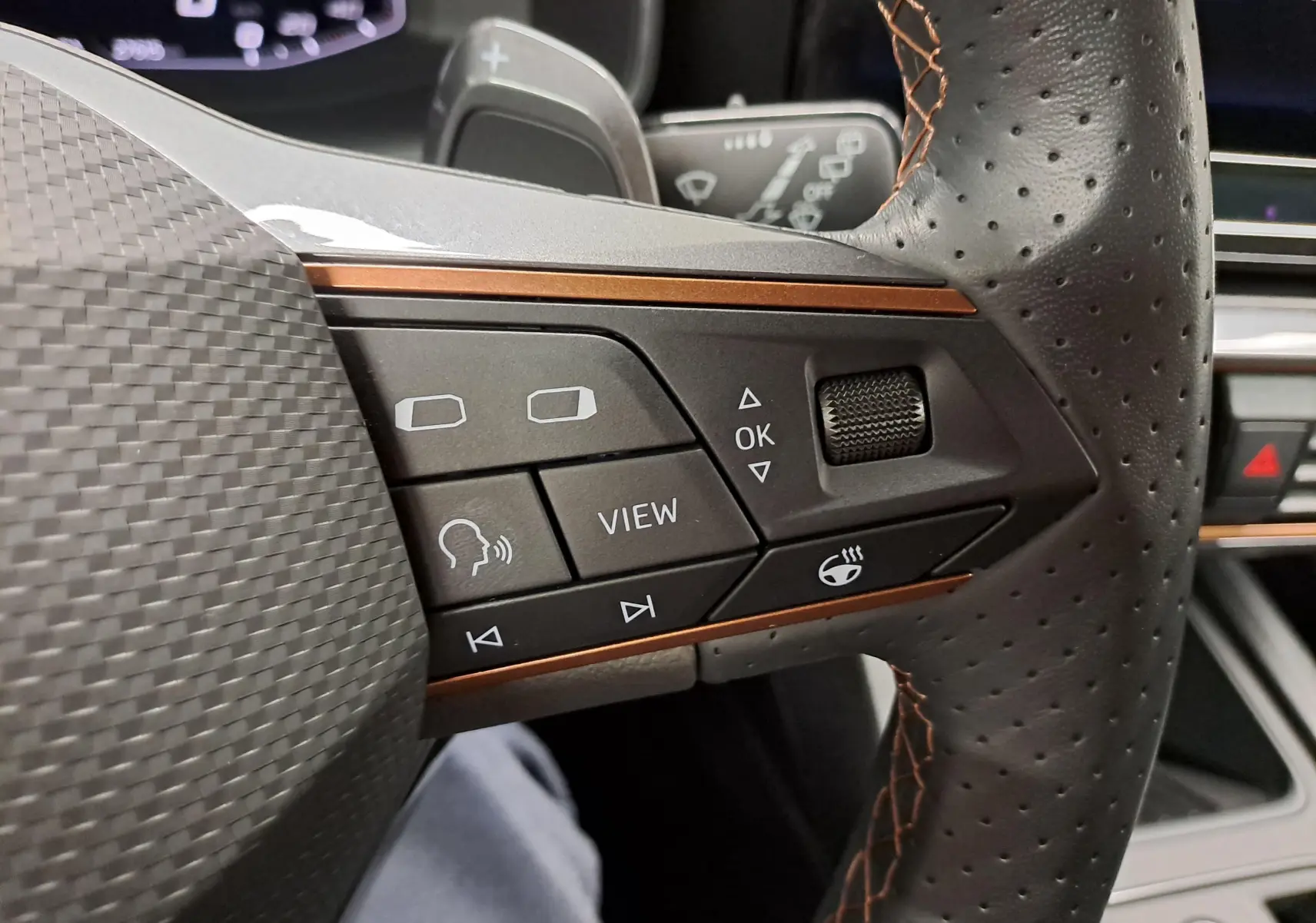 Gros plan sur les commandes à droite du volant perforé avec surpiqûres cuivrées de la CUPRA Leon 2023.