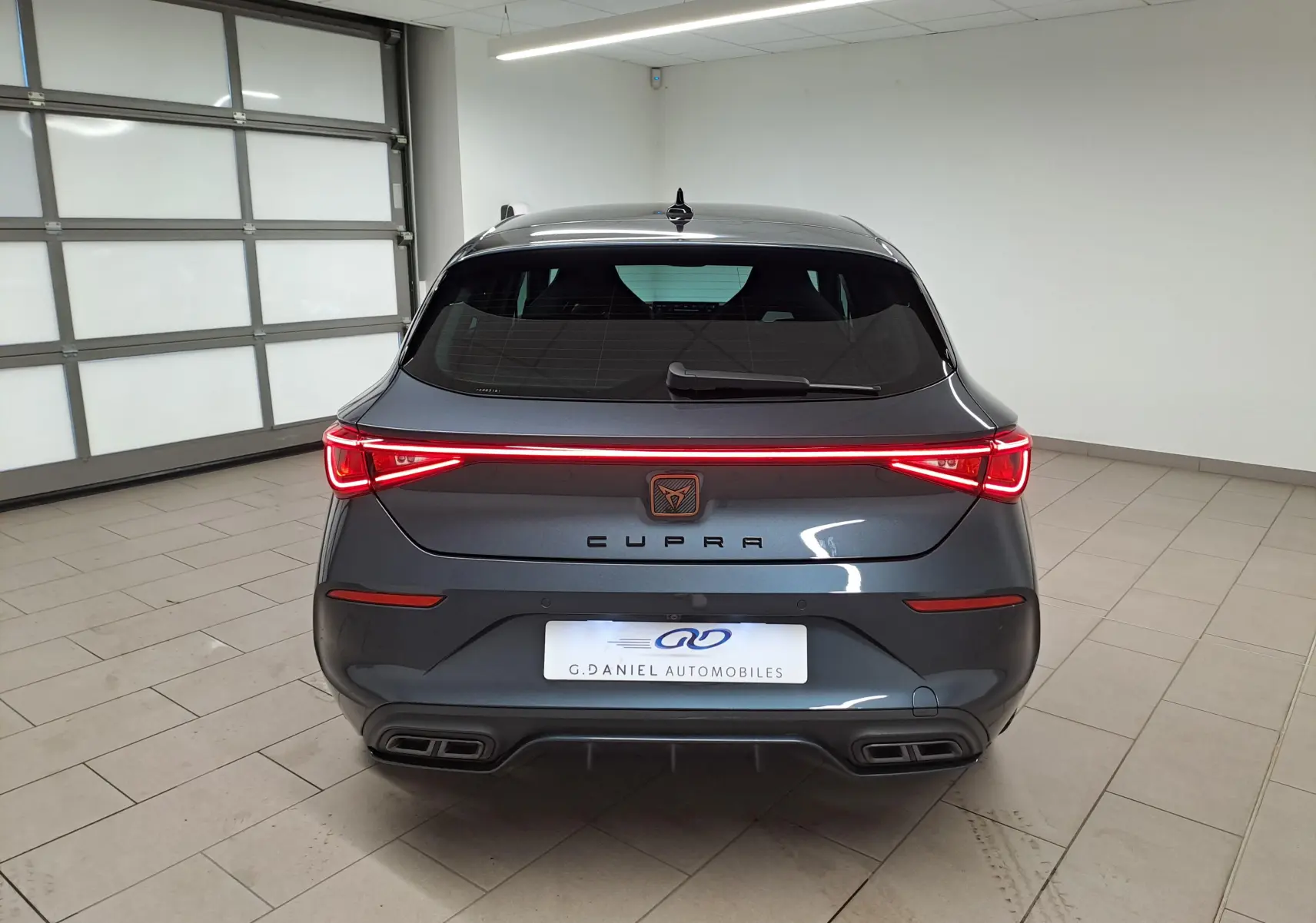 Vue arrière d'une CUPRA Leon 2023 gris magnétique avec feux LED continus et double sortie d'échappement rectangulaire.