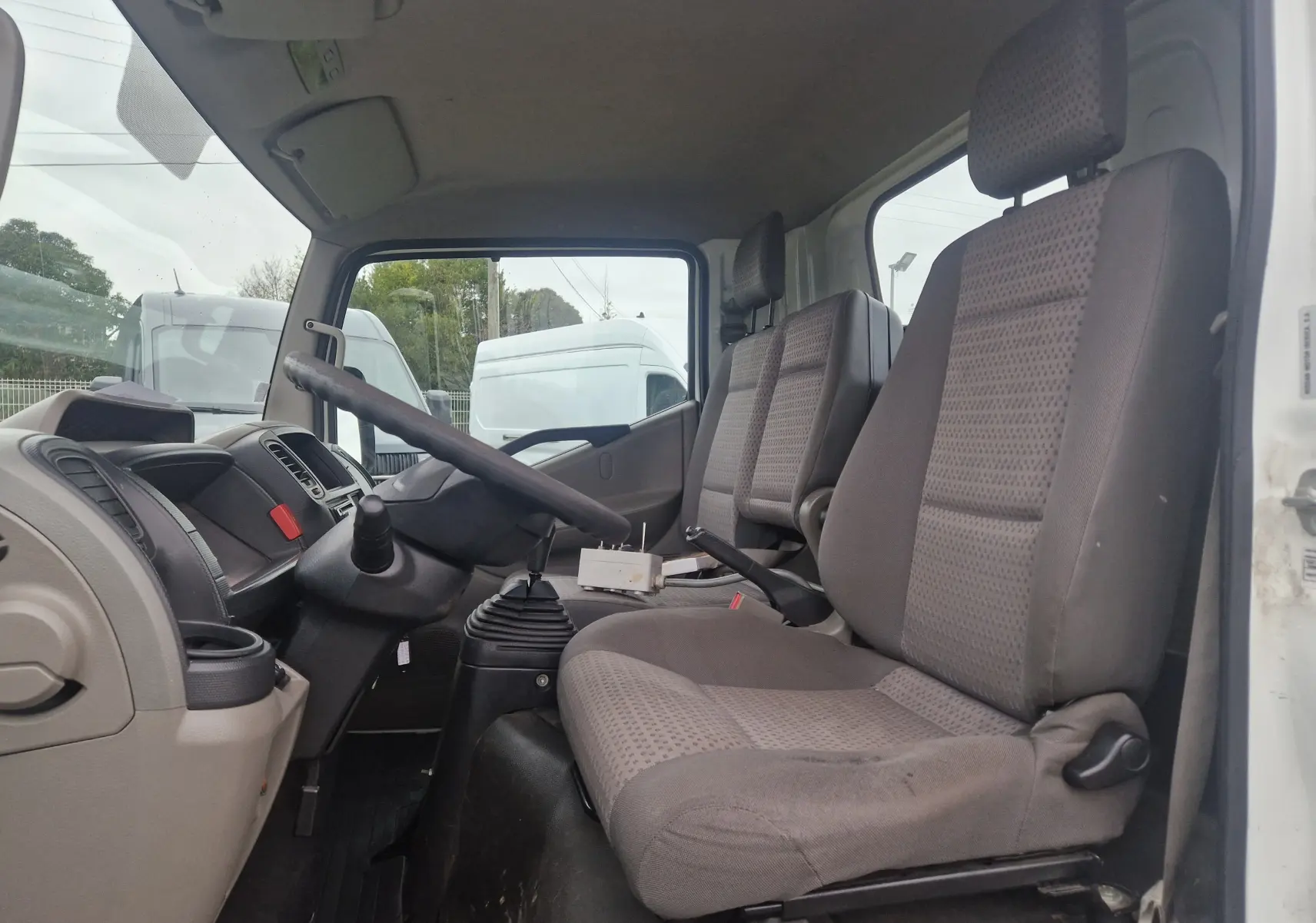 Vue intérieure côté conducteur du Nissan Cabstar blanc 2010, montrant les sièges et le volant avec boîte manuelle.