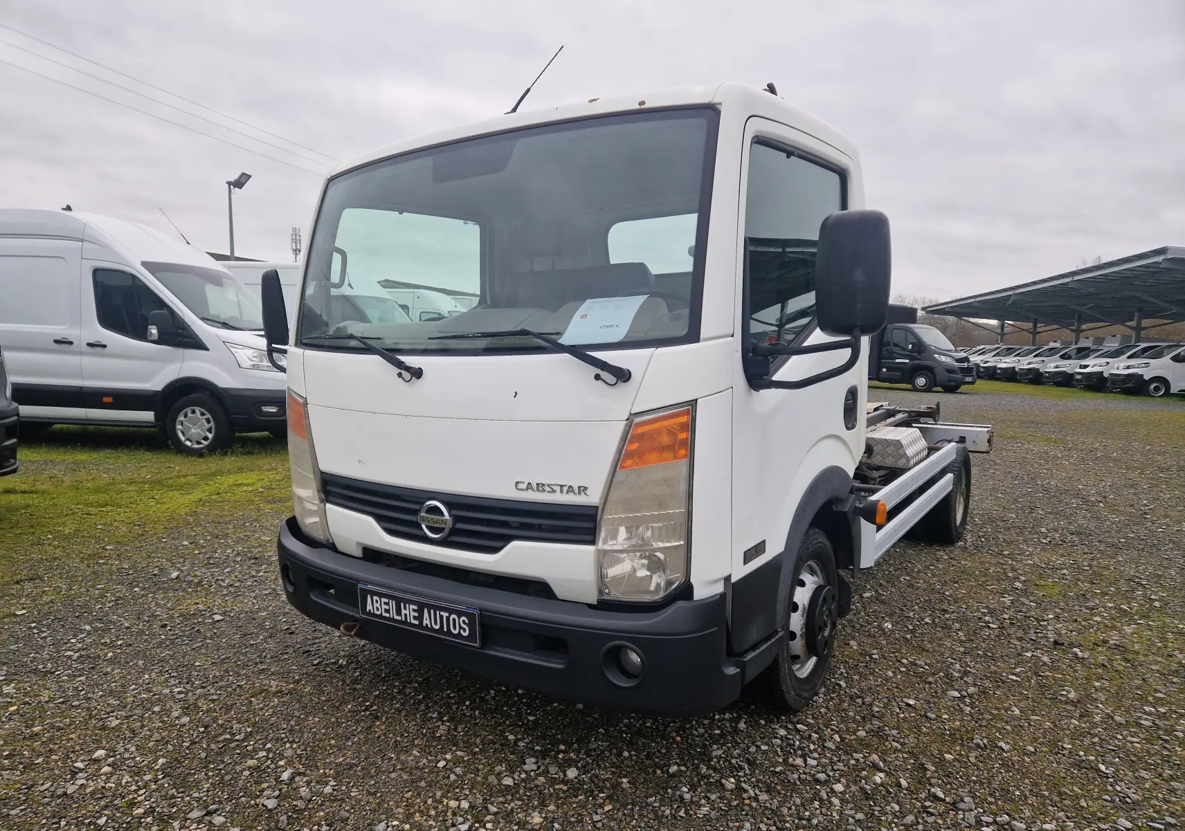Vue 3/4 avant d’un Nissan Cabstar blanc 2010 avec cabine simple et châssis nu, sur un terrain extérieur.