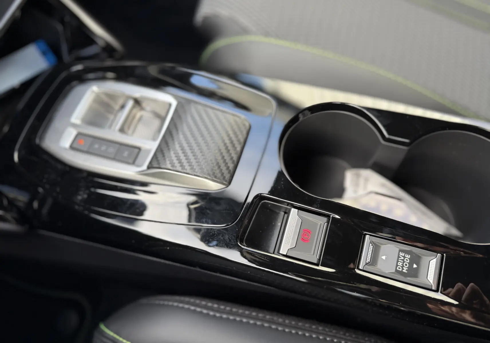 Gros plan sur la console centrale noire brillante du Peugeot 2008 Hybrid 145ch GT avec commandes électroniques et porte-gobelets.