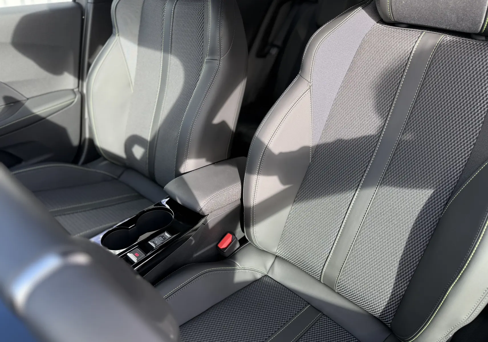 Gros plan sur les sièges avant gris avec surpiqûres vertes du Peugeot 2008 Hybrid 145ch GT 2025, intérieur moderne et soigné.