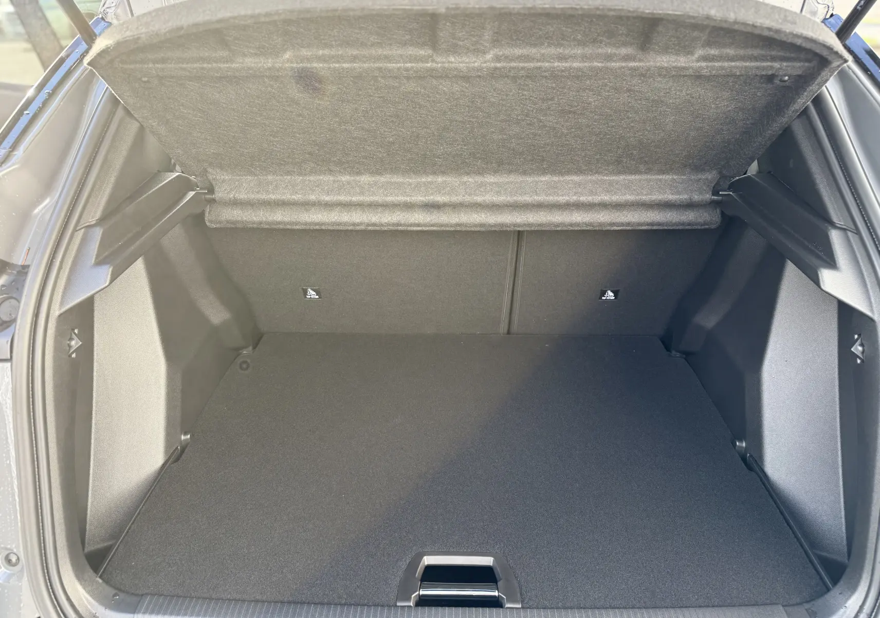 Coffre ouvert vu de l’arrière d’un Peugeot 2008 Hybrid 145ch GT gris Selenium avec toit noir, espace de chargement vide.