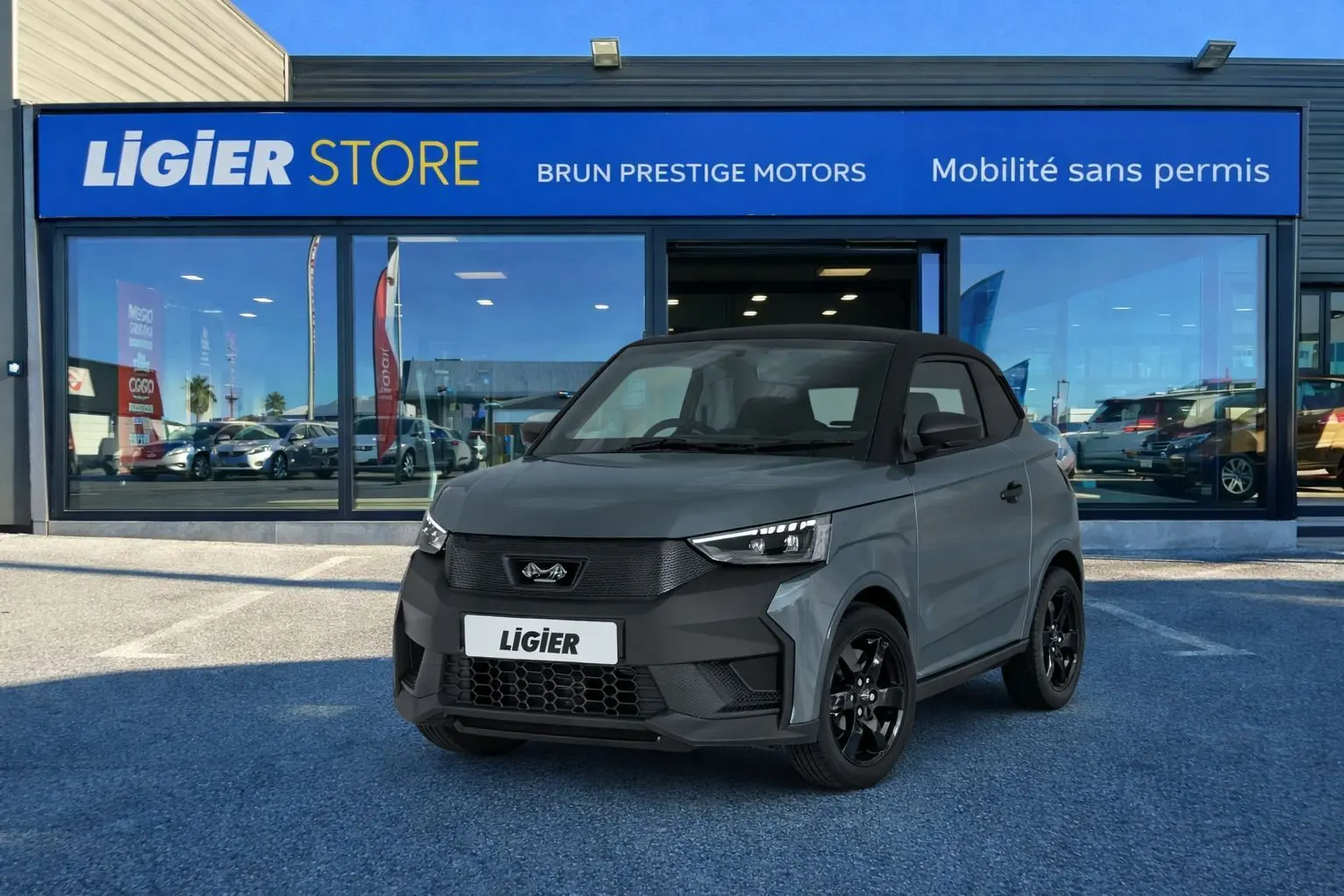 Vue 3/4 avant d'une Ligier JS50 Elite Revo D+ gris graphite avec toit noir, stationnée devant un showroom Ligier.