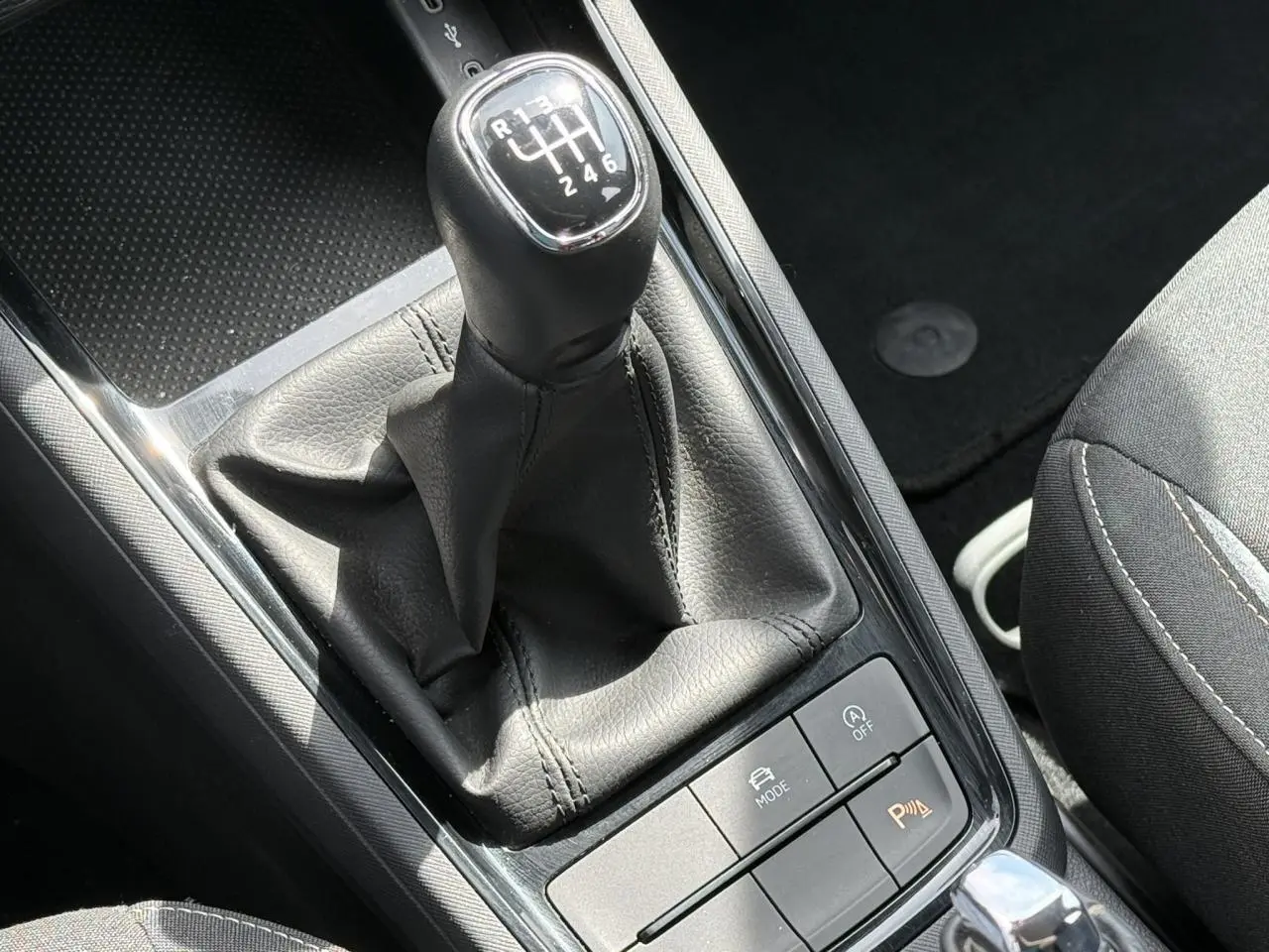 Gros plan sur le levier de vitesses manuel noir de la Skoda Scala TSI 116, entouré de boutons de contrôle sur console centrale.