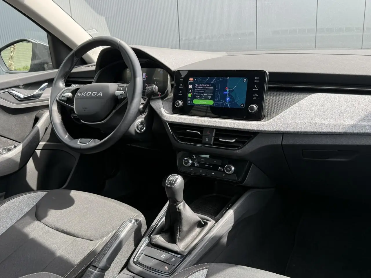 Vue intérieure côté conducteur de la Skoda Scala TSI 116 gris graphite, volant cuir et écran tactile central allumé.