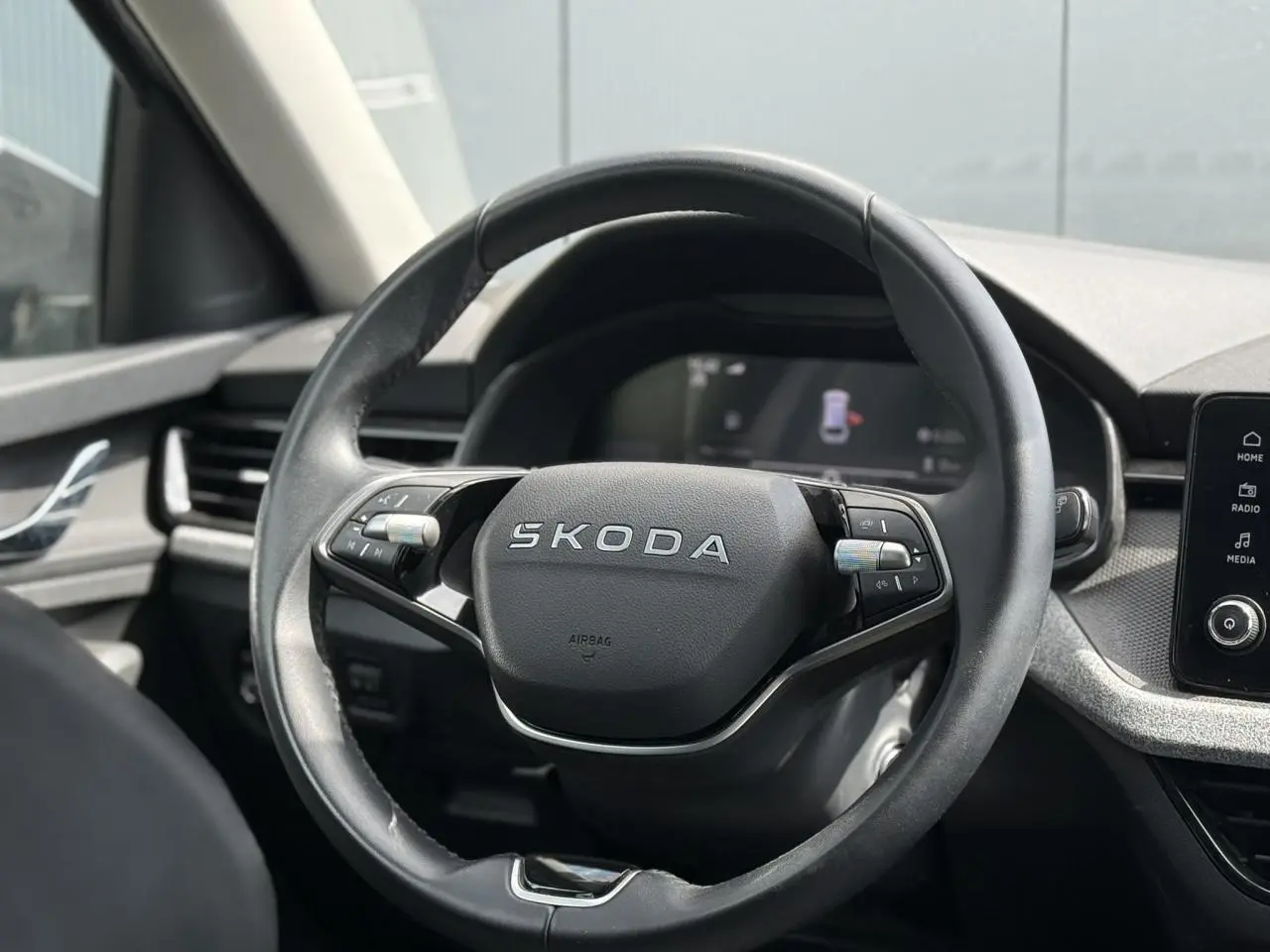 Vue rapprochée du volant en cuir noir avec logo SKODA au centre, tableau de bord et écran tactile visibles en arrière-plan.