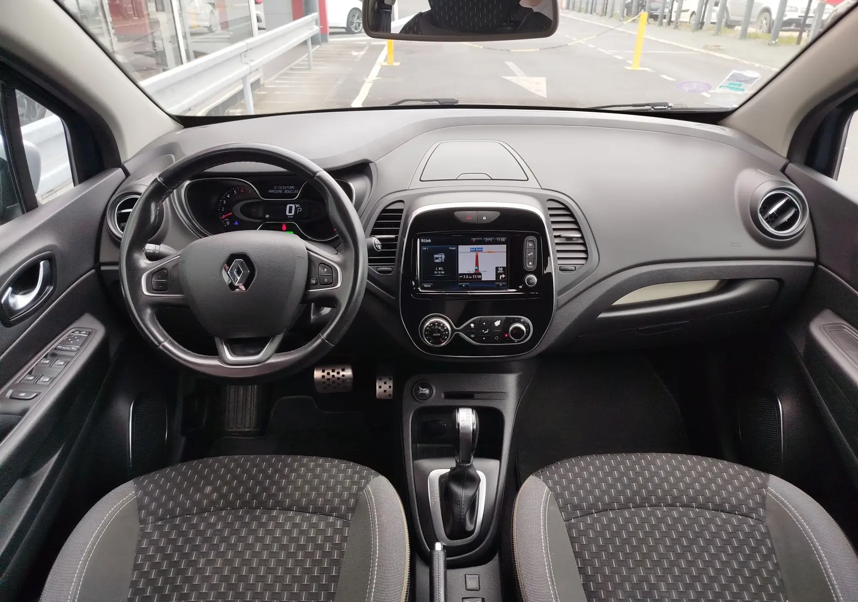 Vue intérieure avant du Renault Captur 2018 montrant le volant, la console centrale avec écran tactile et les sièges gris à motifs.