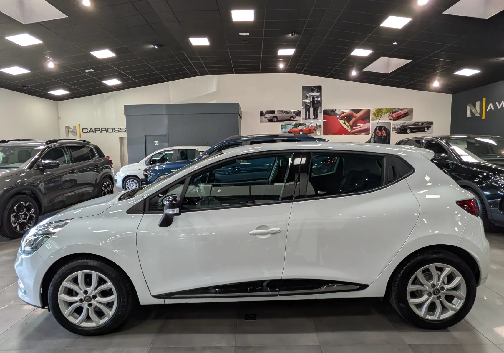 Profil côté gauche d'une Renault Clio IV blanc glacier, version TCe 75 CH GENERATION, en intérieur showroom lumineux.