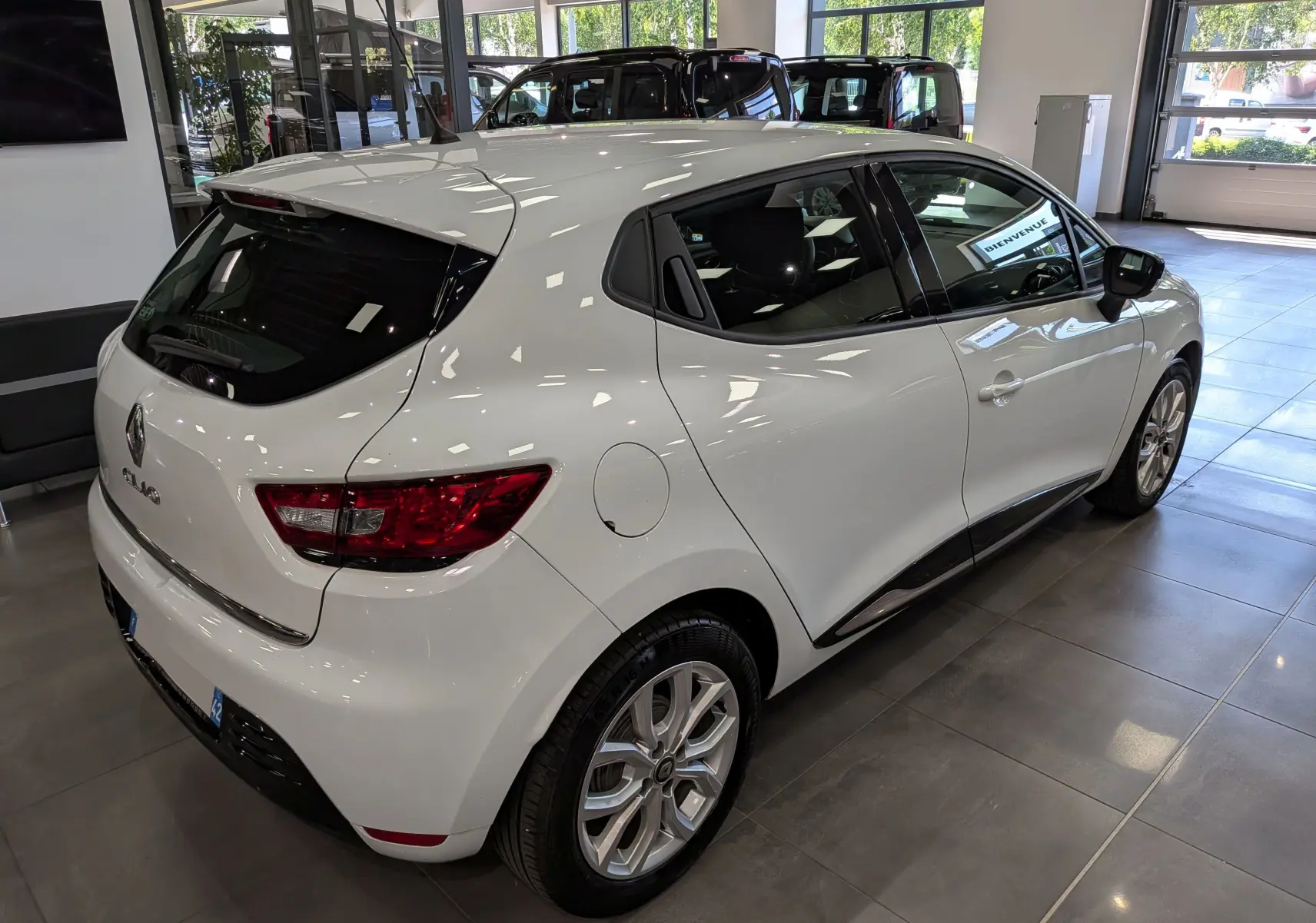 Renault Clio IV TCe 75 blanc glacier vue 3/4 arrière droit en intérieur, avec jantes alliage et vitres teintées.