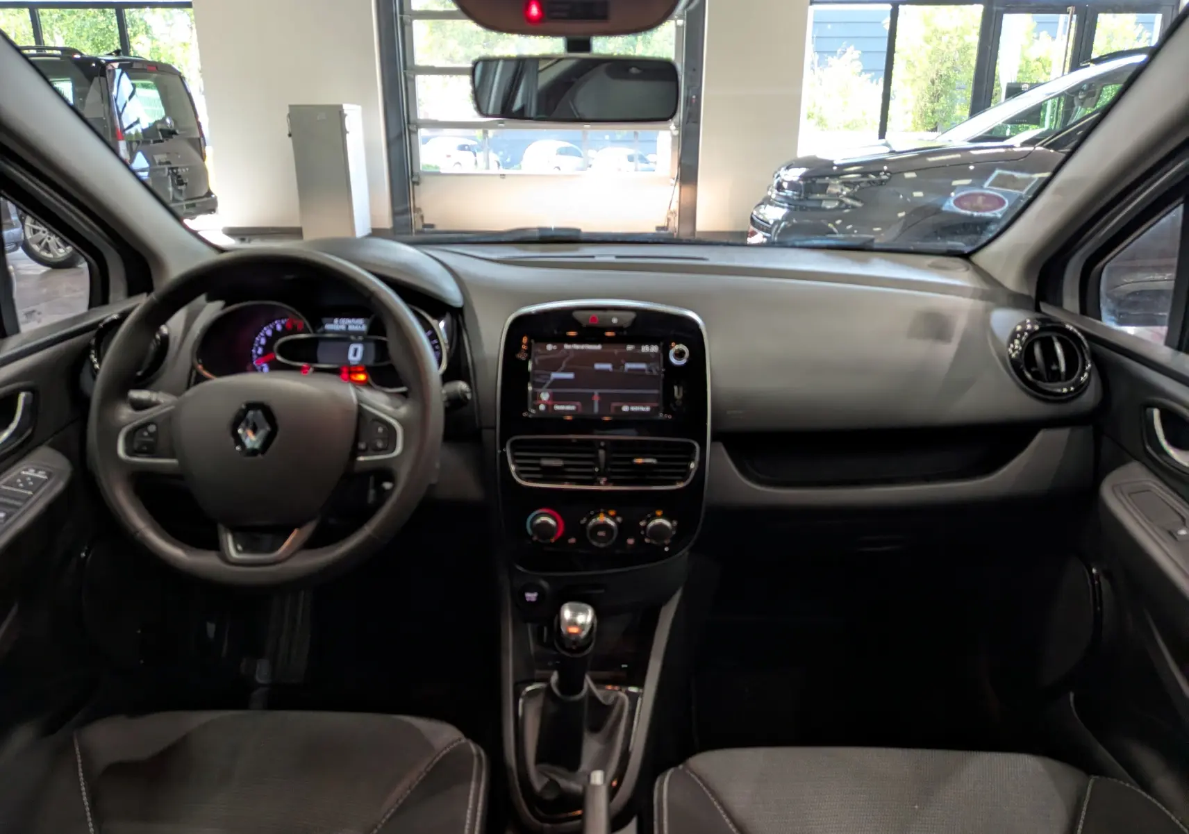 Vue intérieure frontale du tableau de bord et volant de la Renault Clio IV TCe 75 blanche avec écran tactile et boîte manuelle.