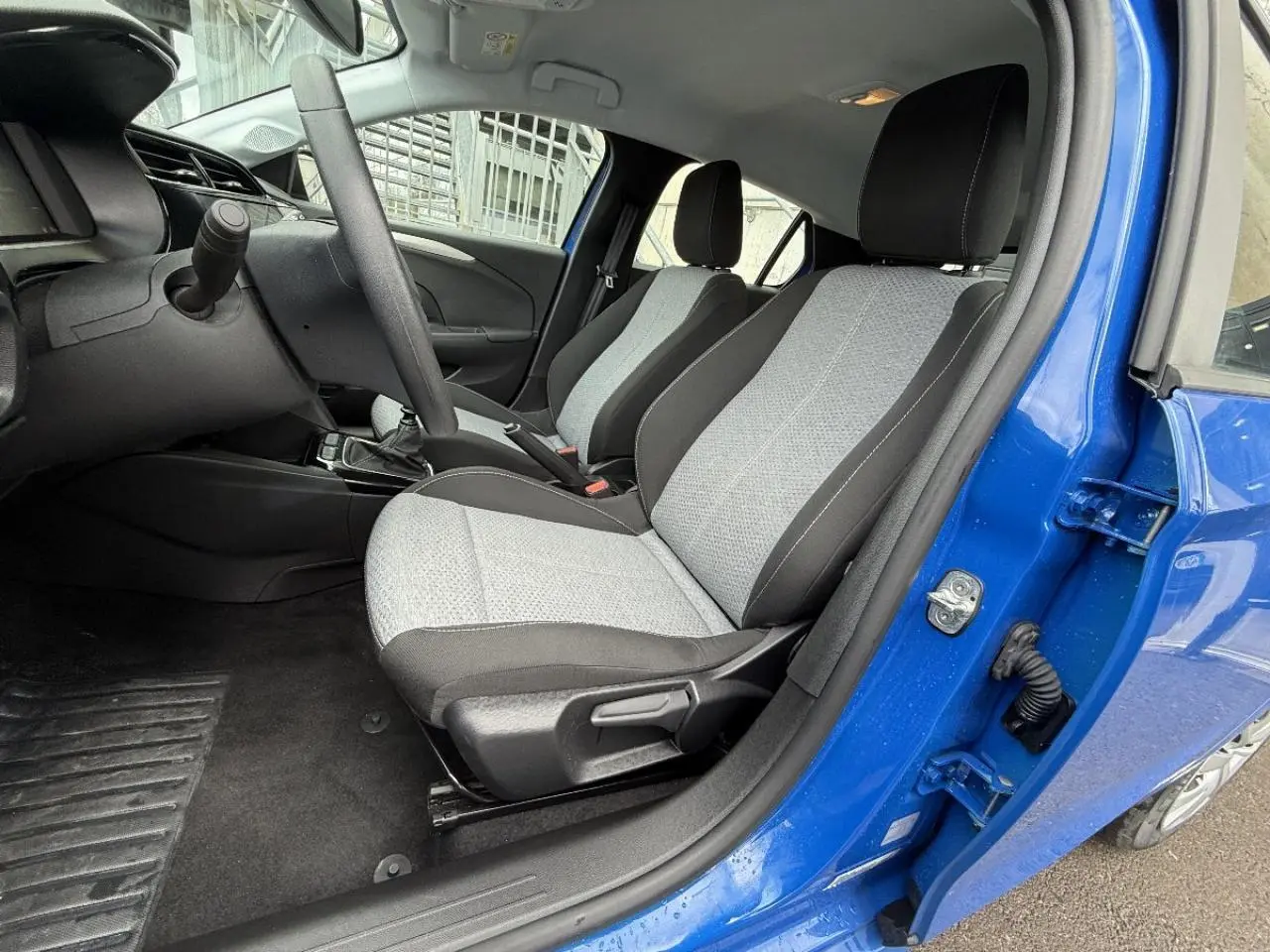 Intérieur avant droit de l’Opel Corsa 2025 bleu voltaik, montrant les sièges gris et noir et la boîte manuelle.