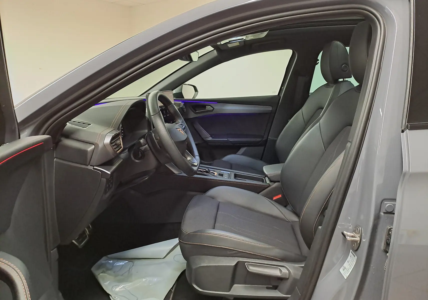 Vue intérieure côté conducteur de la CUPRA LEON ST gris Graphène, sièges noirs avec surpiqûres cuivrées et toit ouvrant panoramique visible.