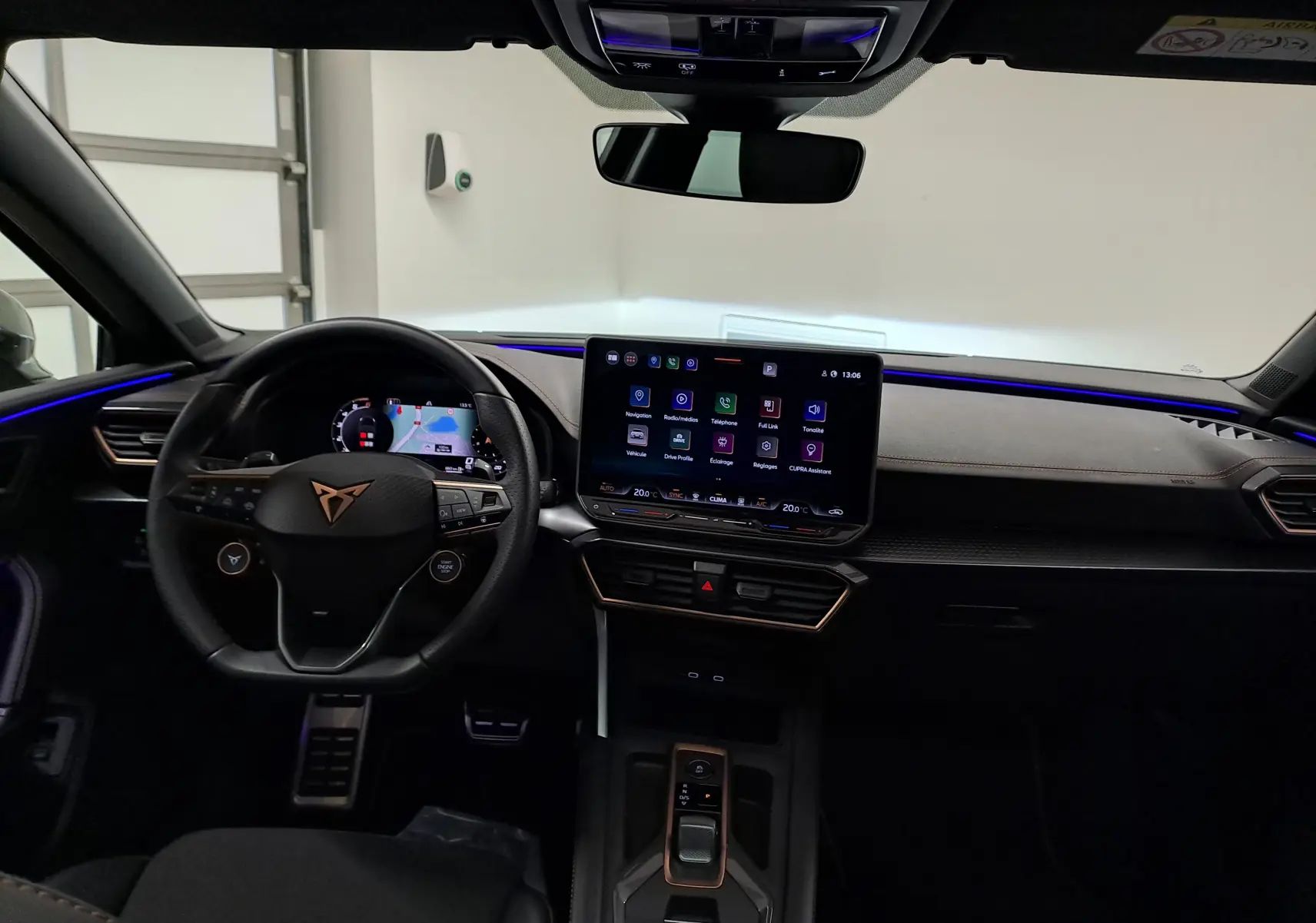 Vue intérieure du tableau de bord de la CUPRA LEON ST 2025 avec écran tactile central et éclairage d’ambiance bleu.