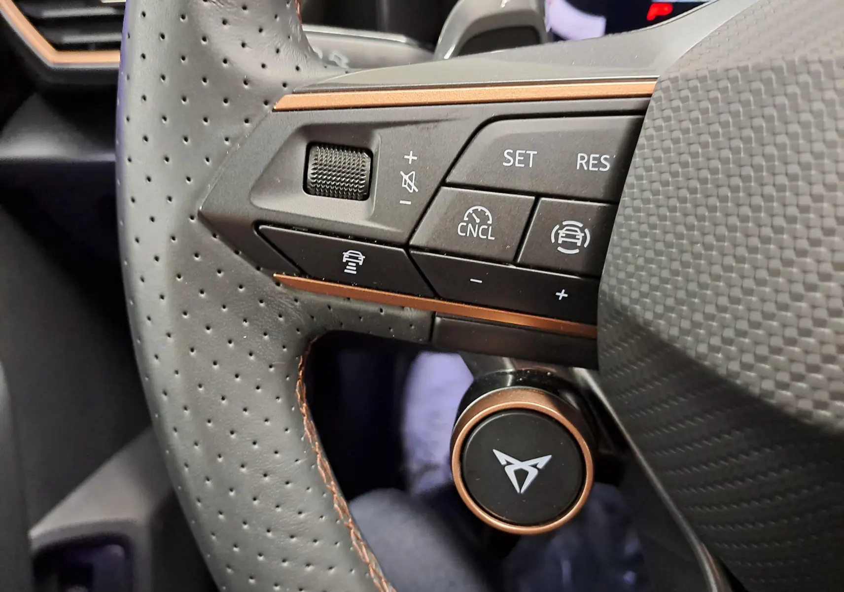 Gros plan sur la partie gauche du volant perforé avec surpiqûres cuivrées du CUPRA Leon ST gris Graphène, boutons de commande intégrés.