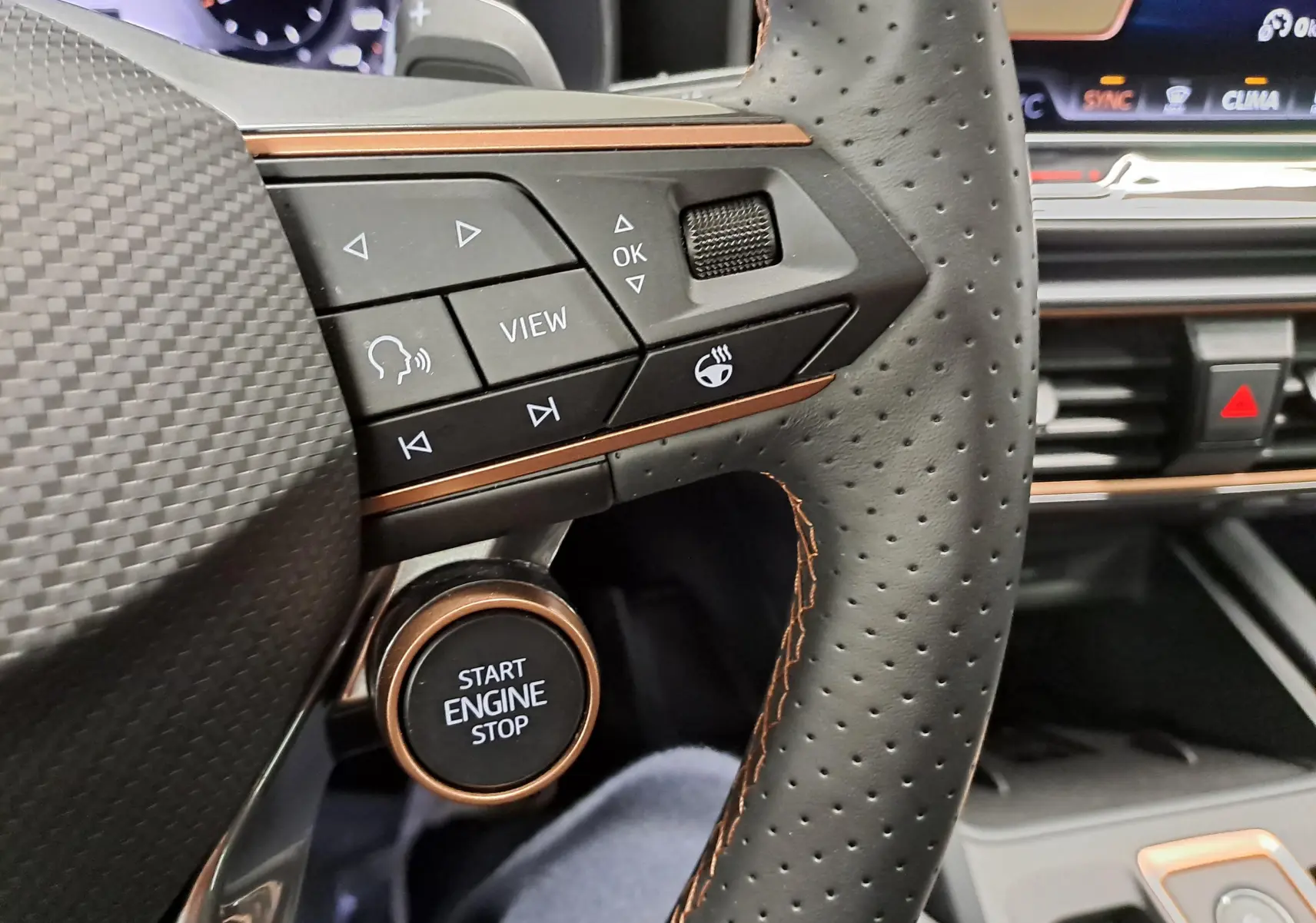 Gros plan sur le volant perforé avec commandes intégrées et bouton start/stop cuivré du CUPRA LEON ST 2025.