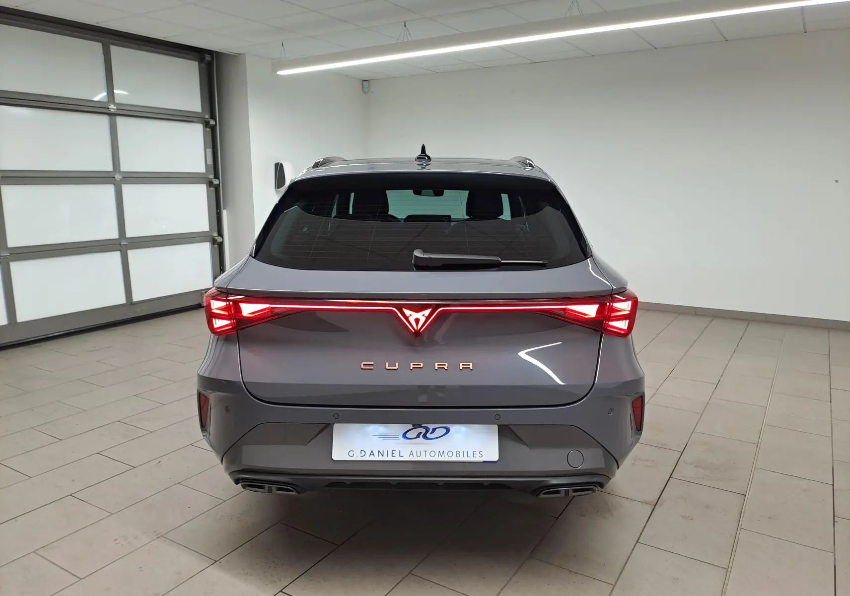 Vue arrière d'une CUPRA LEON ST 2.0 TDI 150 DSG7 en gris Graphène avec feux arrière allumés dans un garage.
