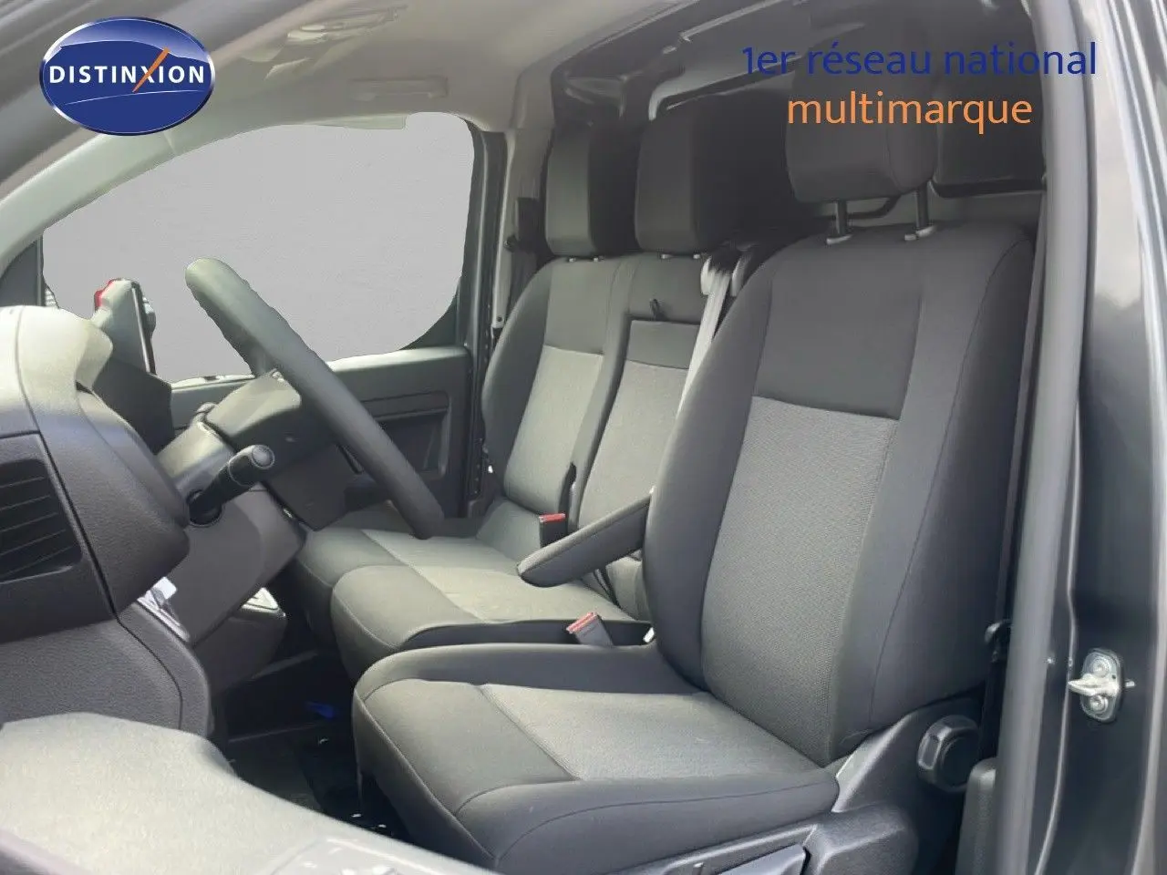 Vue intérieure côté conducteur du Citroën Jumpy gris titane, montrant les sièges avant en tissu noir et gris.