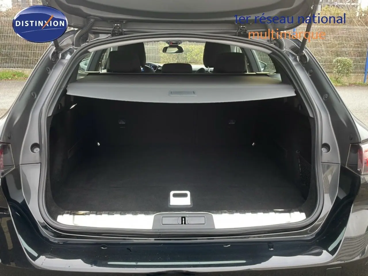 Coffre ouvert vu de l'arrière d'une Peugeot 508 SW noire Perla Nera, espace de chargement spacieux et tapis noir.