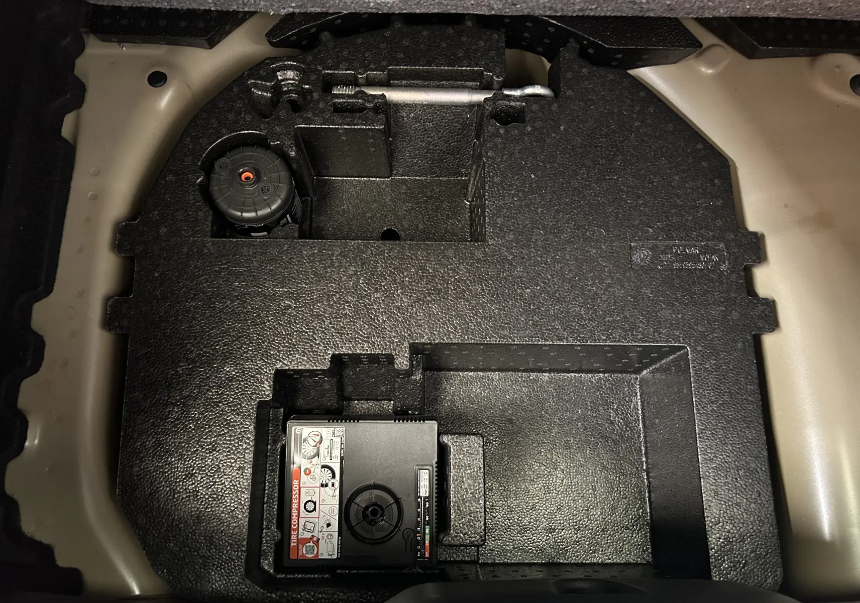 Vue rapprochée du compartiment de rangement sous le coffre d'une Citroën C3 gris Artense, montrant le compresseur de pneu intégré.