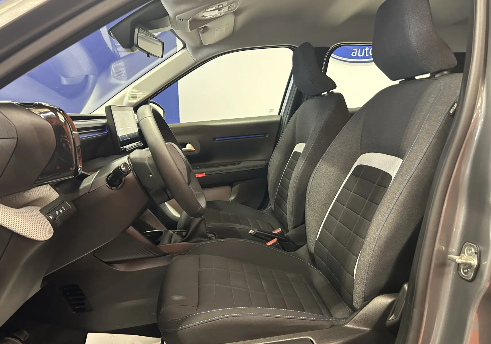 Vue intérieure côté conducteur de la Citroën C3 2025 gris Artense, sièges tissu noir avec surpiqûres bleues et tableau de bord moderne.