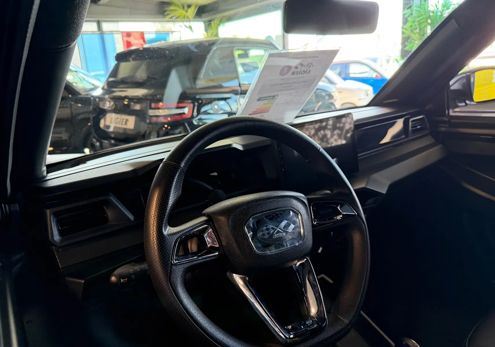 Vue intérieure centrée sur le volant noir du Ligier JS50 Select Revo D+ avec tableau de bord moderne et vitre avant lumineuse.