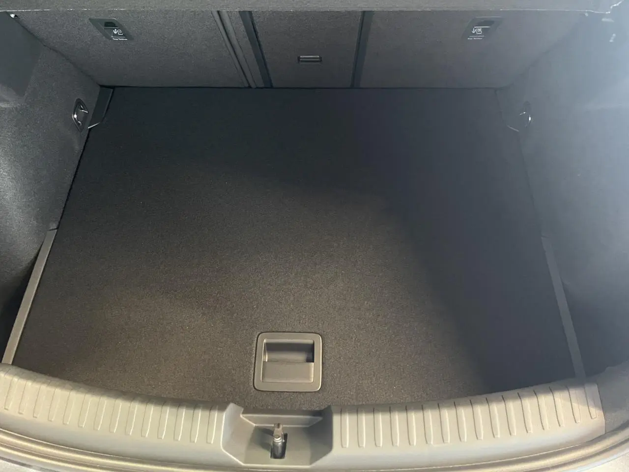 Coffre vide vu de dessus de la CUPRA Leon 1.5 eTSI Hybrid gris, avec tapis de sol noir et poignées intégrées.