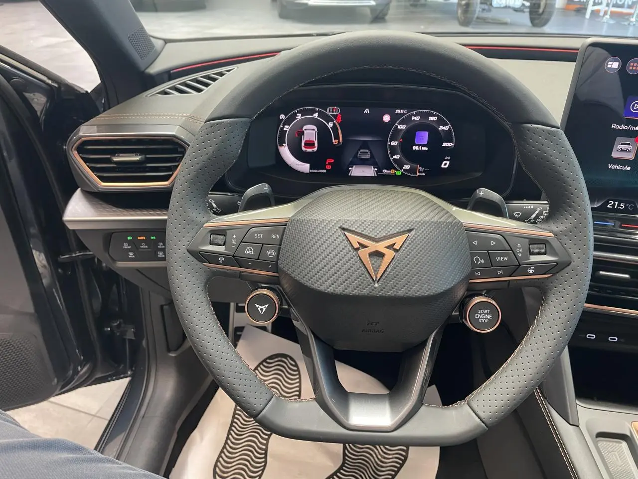 Vue intérieure centrée sur le volant perforé noir avec logo cuivré et tableau de bord digital de la CUPRA Leon 2026.