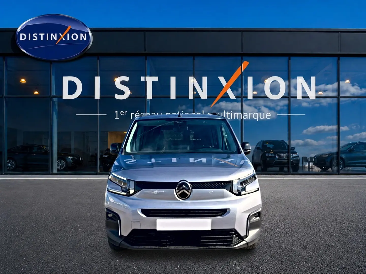 Vue frontale d'un Citroën Berlingo 2026 gris acier, avec calandre distinctive et phares LED devant un showroom Distinxion.