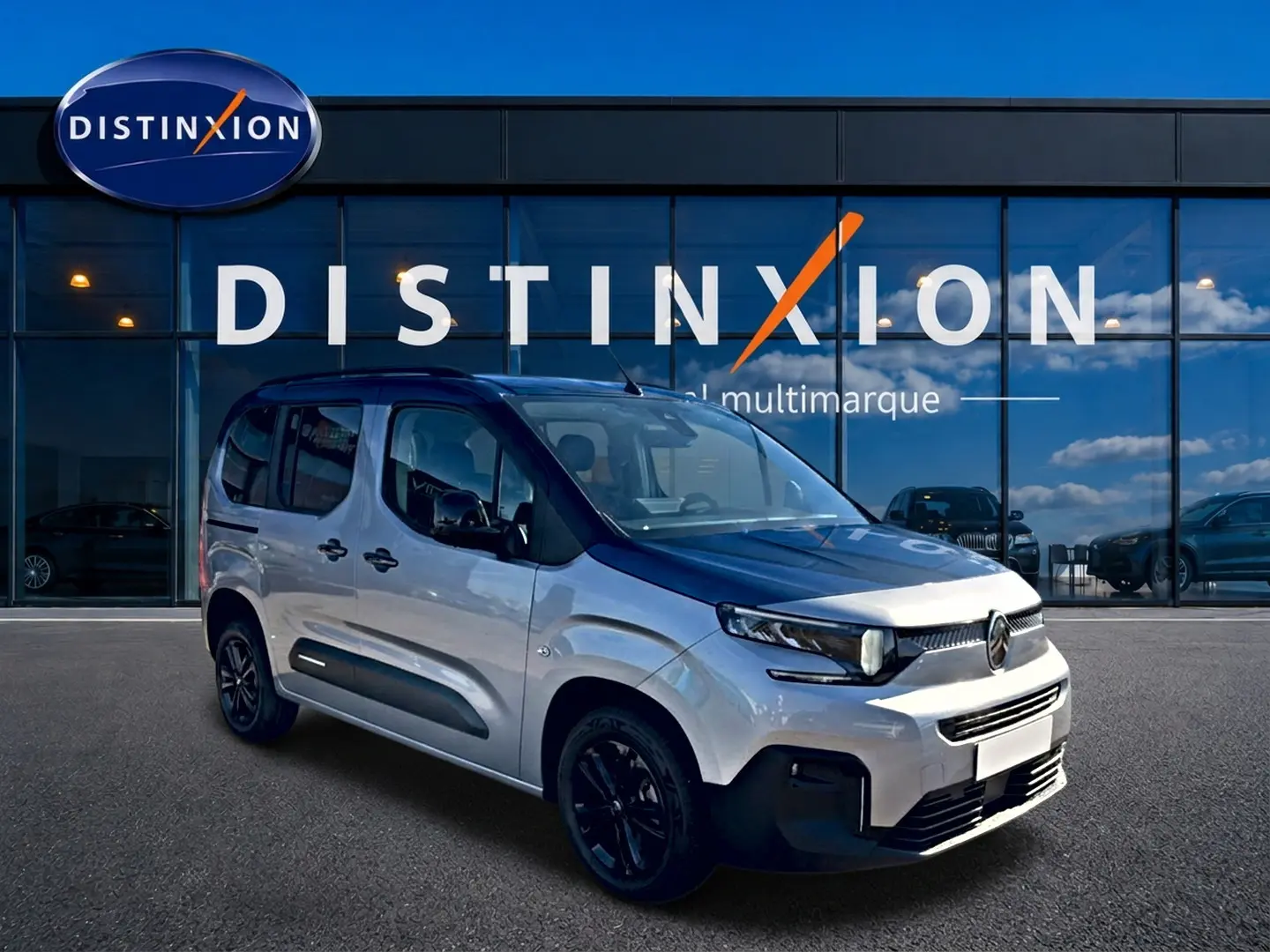 Vue 3/4 avant droit du Citroën Berlingo gris acier avec jantes noires, devant une vitrine Distinxion.