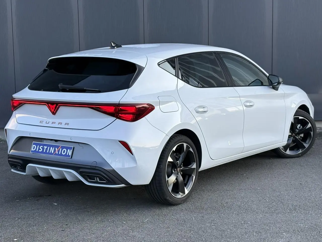 Vue 3/4 arrière droite de la CUPRA Leon blanche Neige avec jantes alliage 18'' et bandeau lumineux arrière Tri-LED.