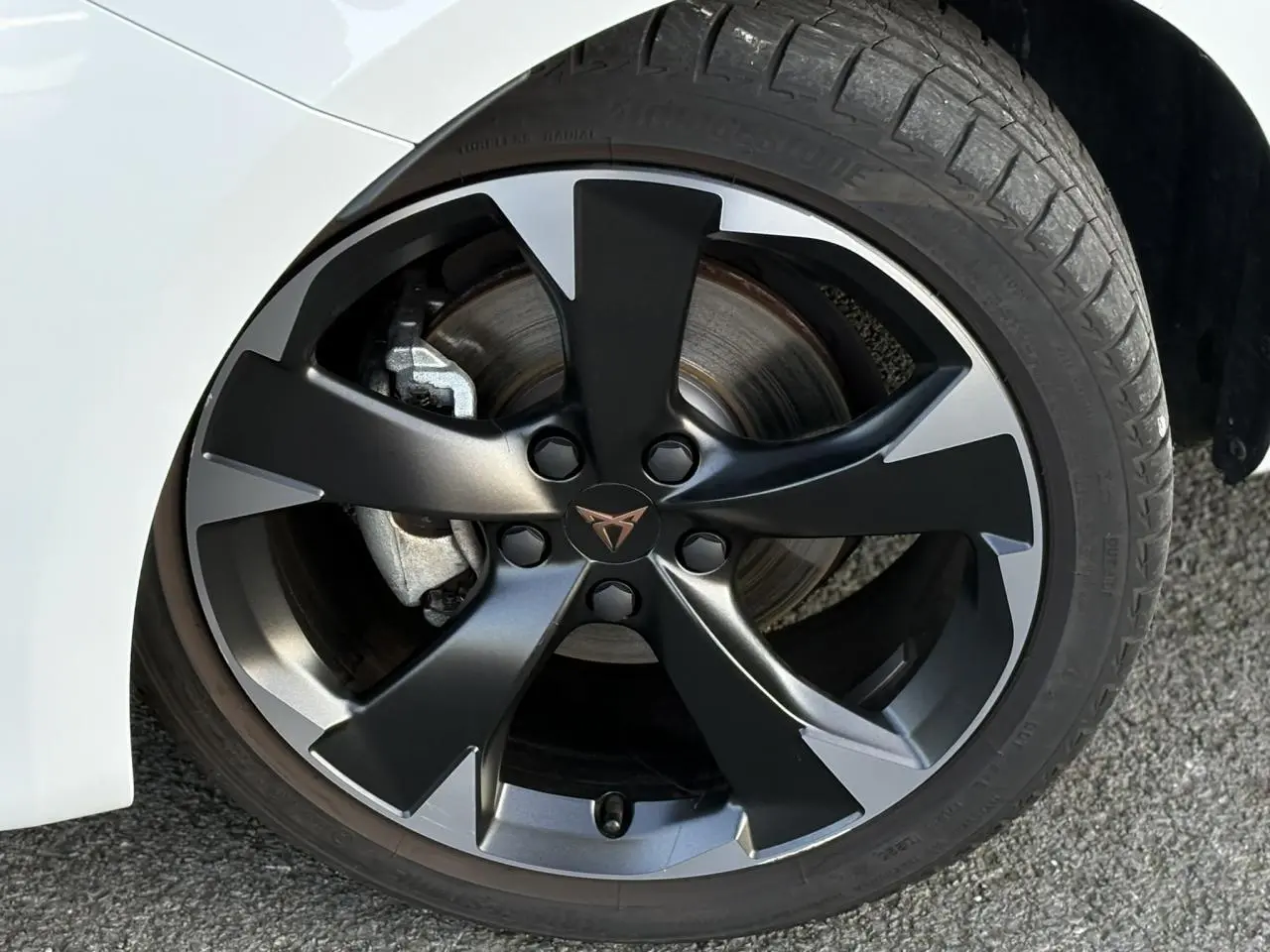 Gros plan sur la jante alliage 18'' bicolore noire et grise de la CUPRA Leon Blanc Neige, avec logo CUPRA central.