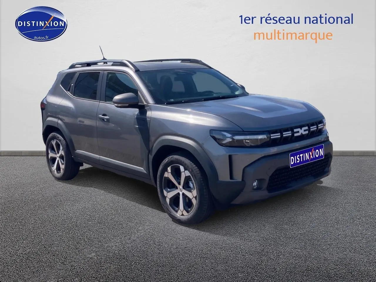 SUV Dacia Duster gris schiste en 3/4 avant droit, avec barres de toit et jantes alliage visibles.