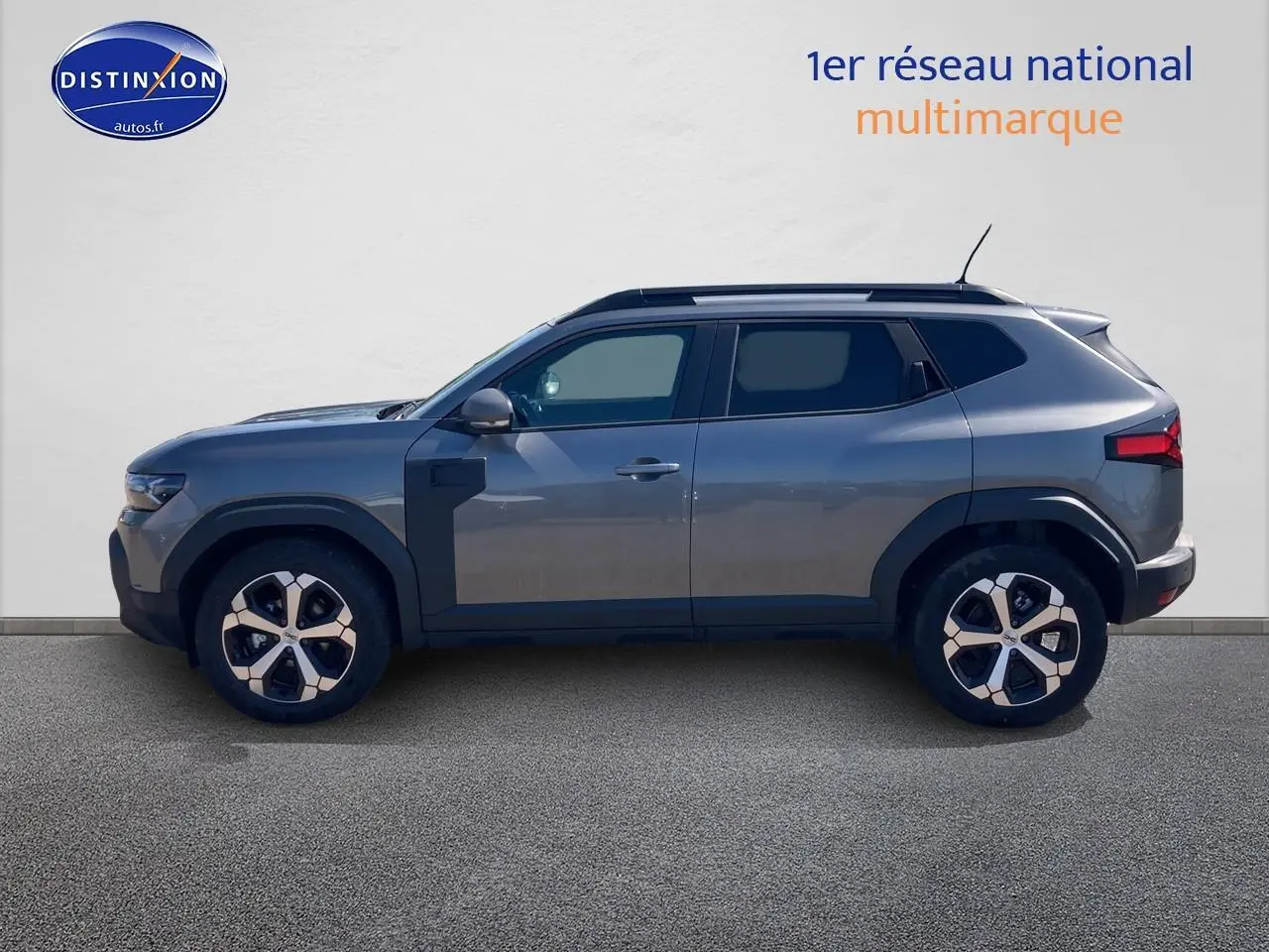 Profil droit du Dacia Duster 1.2 mild hybrid 140 Journey gris schiste avec jantes alu et barres de toit visibles.
