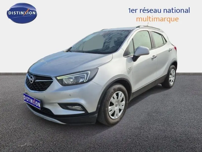 Opel Mokka X gris minéral vu en 3/4 avant droit, avec barres de toit et jantes acier.