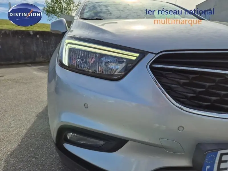 Gros plan sur l'avant gauche gris minéral de l'Opel Mokka X, mettant en valeur le phare LED et la calandre chromée.