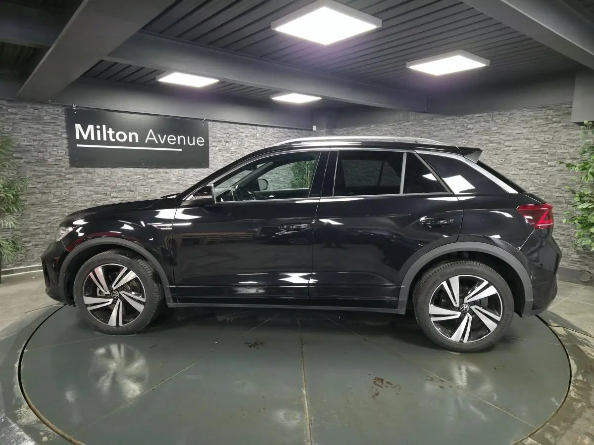 Profil droit d’un Volkswagen T-Roc noir 2023 R-Line avec jantes alliage et vitres arrière surteintées dans un showroom.